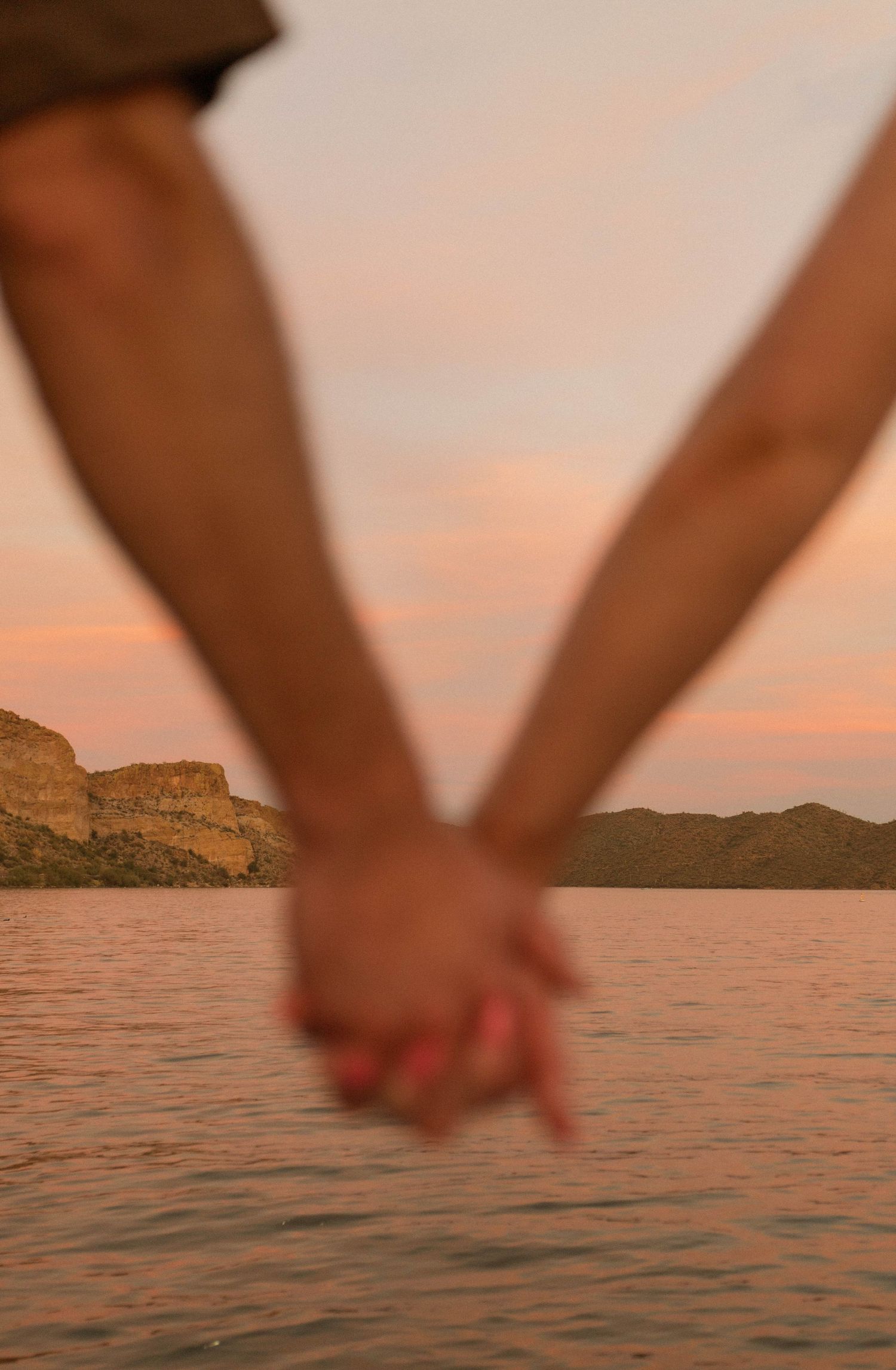 Two hands joined together against a sunset lake backdrop with desert mountains in the distance.
