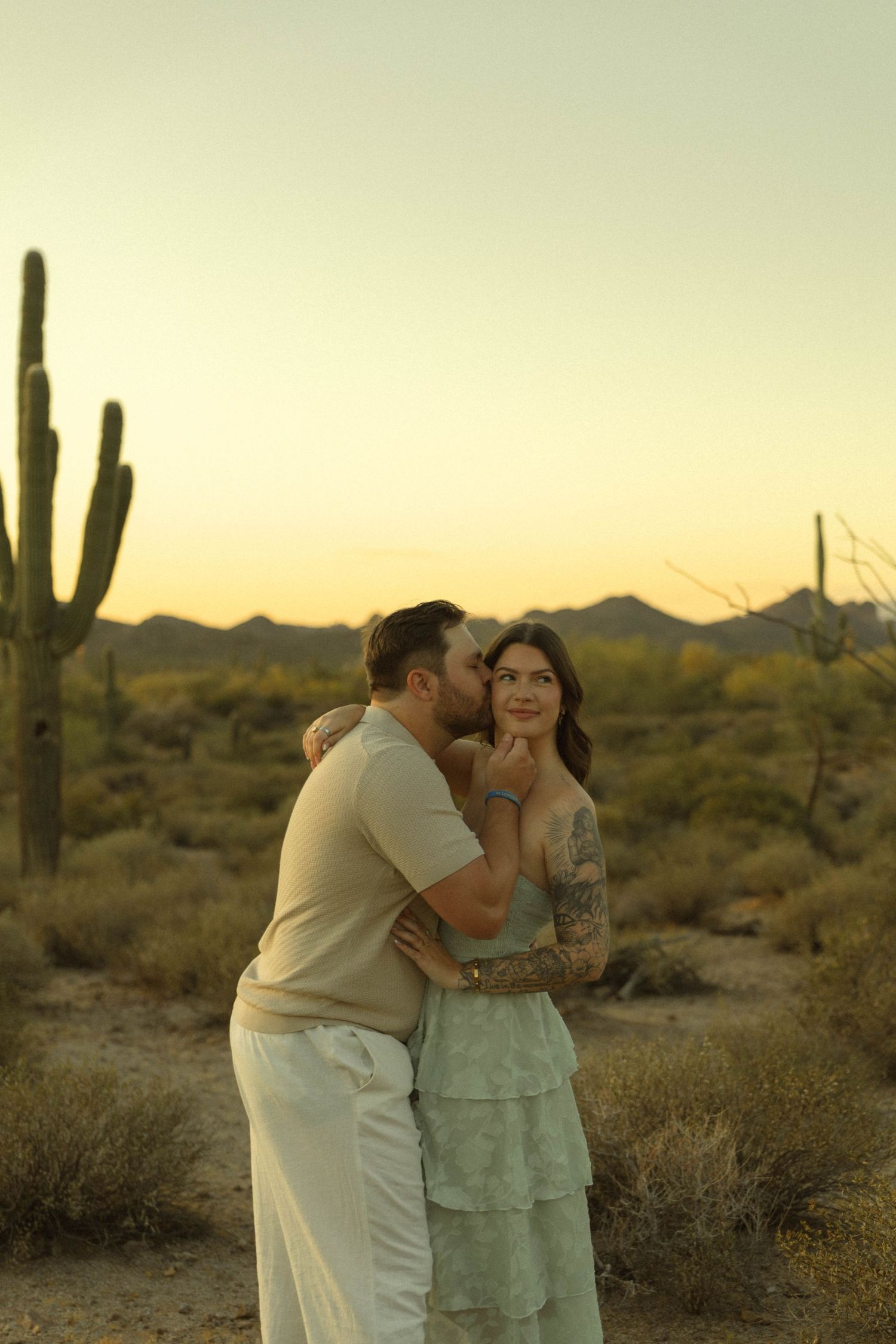 Couple embracing at golden hour in Arizona desert with saguaro cacti backdrop.