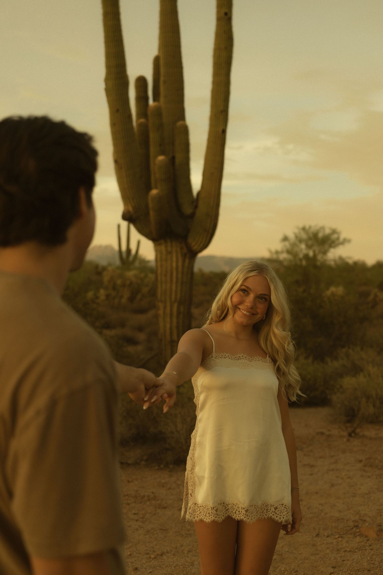 Couple holding hands in Arizona desert at golden hour with saguaro cactus backdrop.