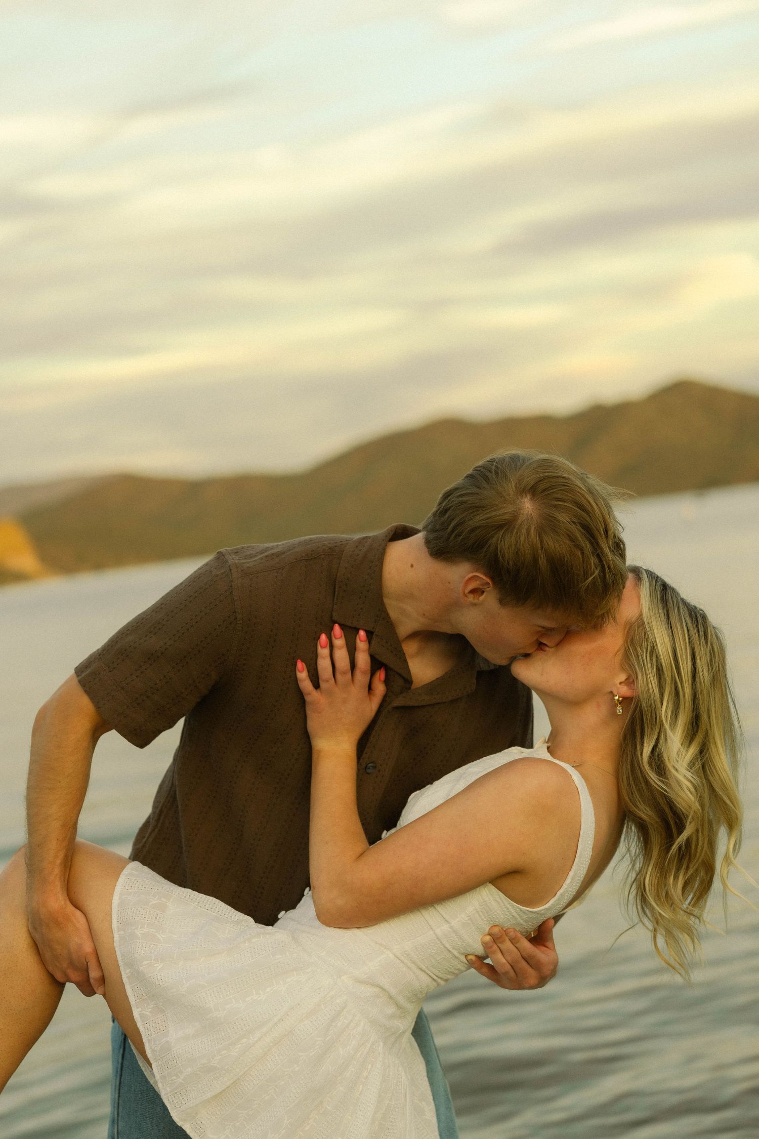 A passionate embrace photographed at sunset with mountains and water in the background.