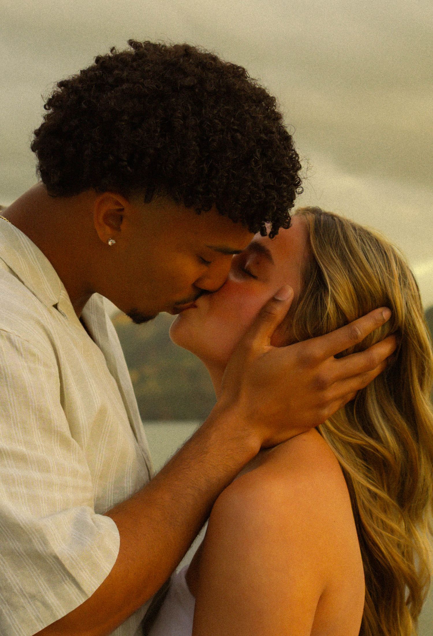 An intimate moment between a couple sharing a tender kiss against a warm neutral background.