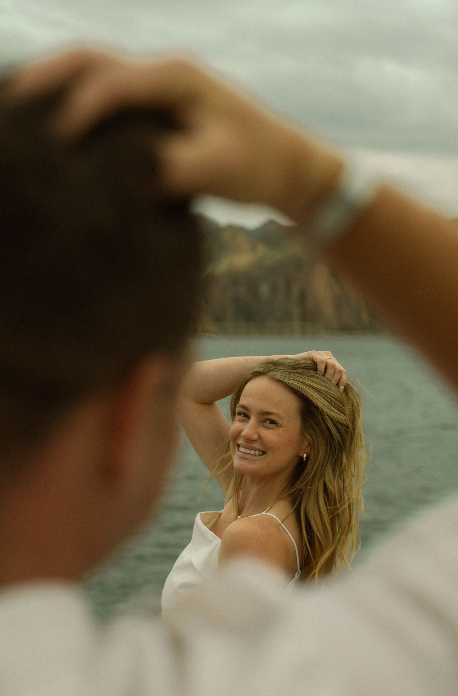 A couple shares candid moments on a dock with dramatic mountain scenery in the background.