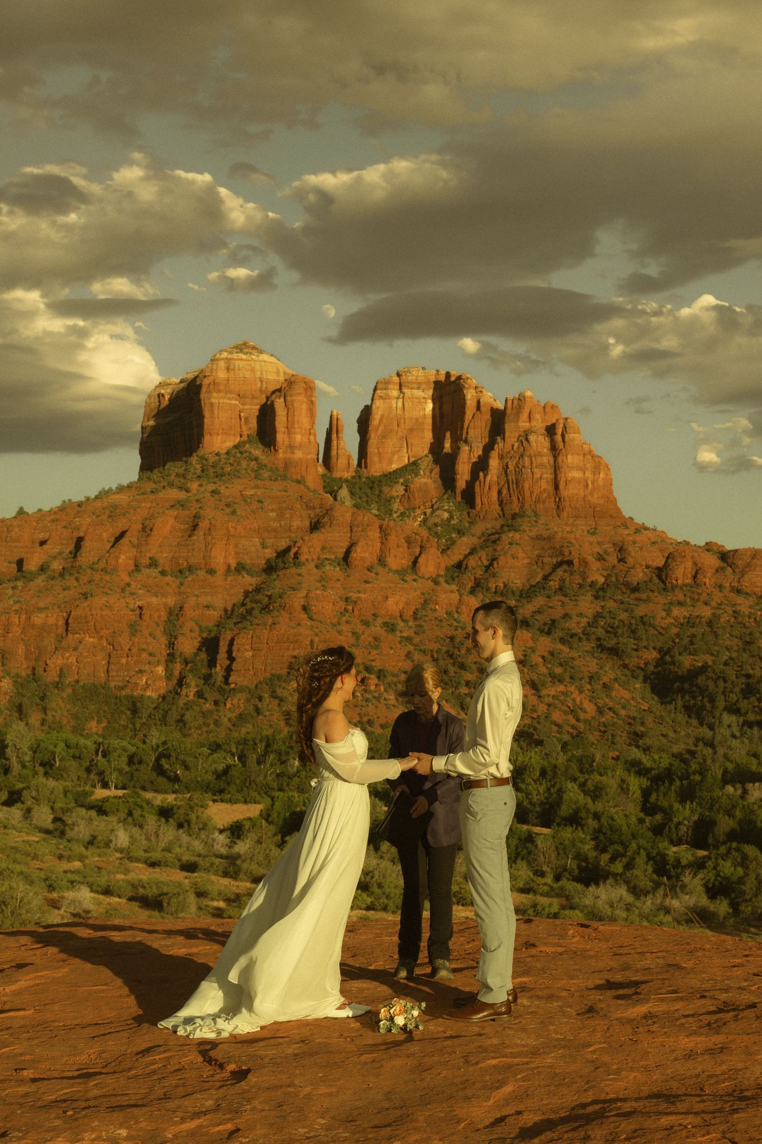 Couple exchanges wedding vows at sunset on red rocks in Sedona, Arizona, with Cathedral Rock formation in the background.