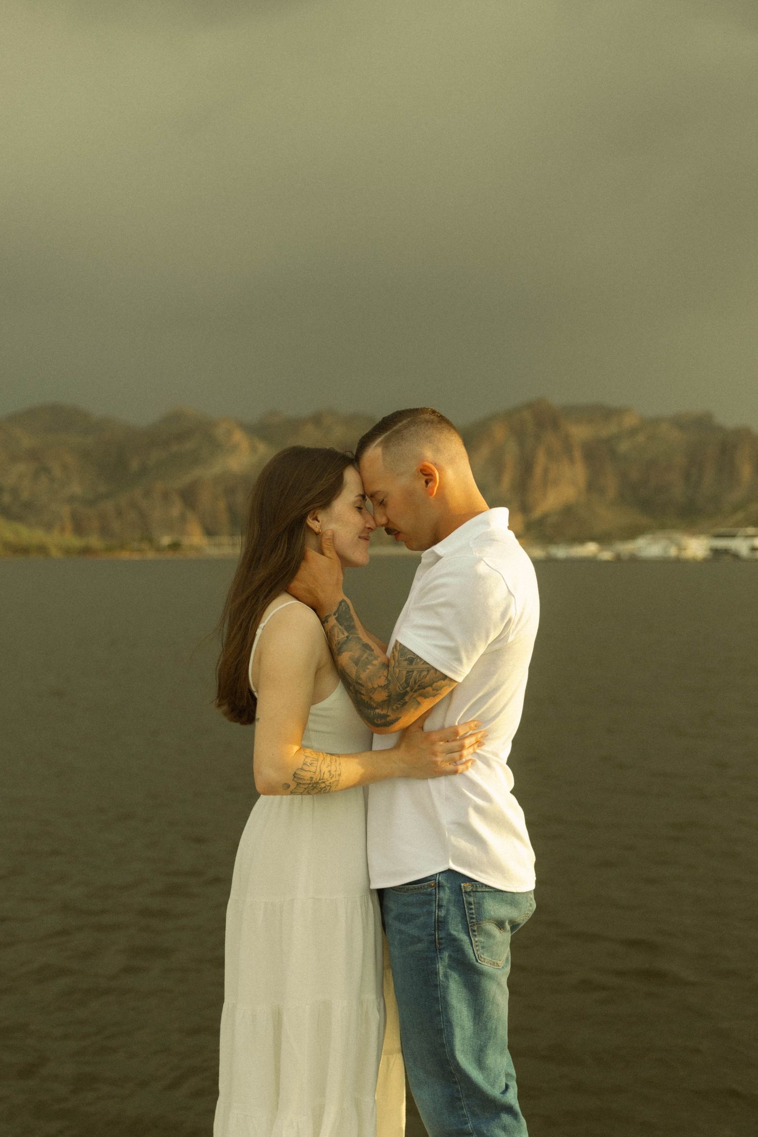 A romantic couple embraces against a backdrop of rugged coastal cliffs during golden hour.