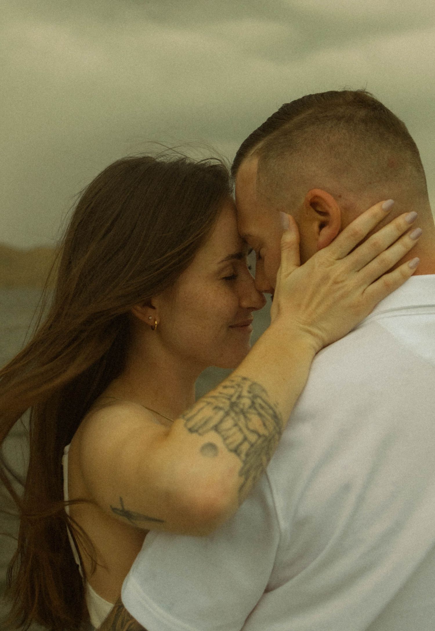 An intimate moment captured between a couple embracing outdoors with a moody sky in the background.