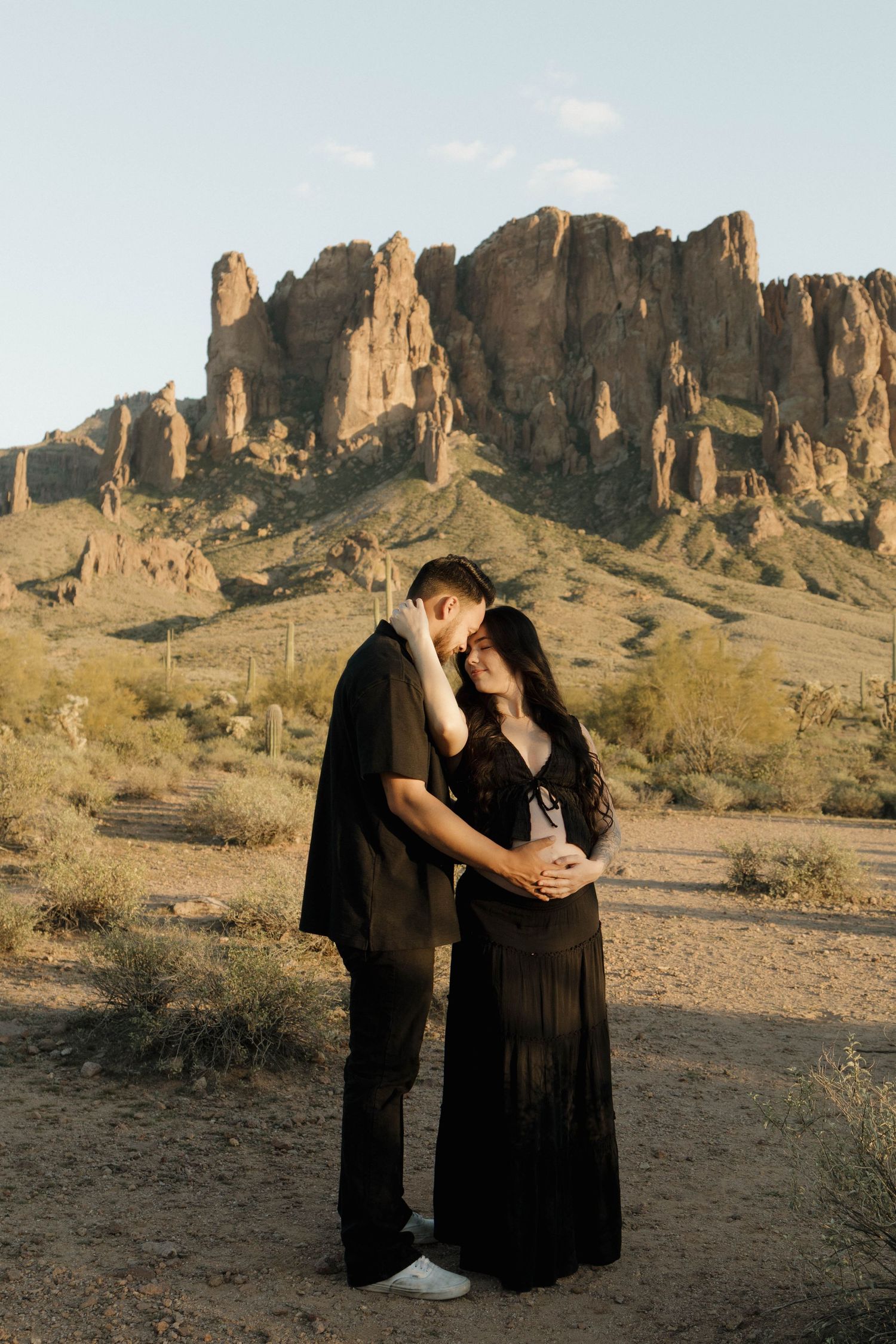 A couple shares intimate moments in a desert landscape with dramatic rock formations at sunset.