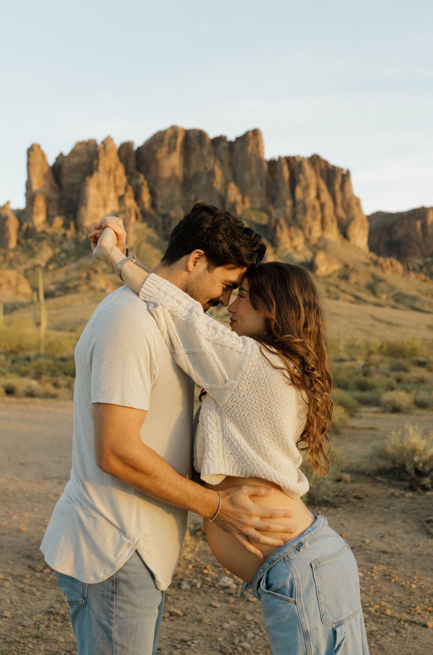 Two people embrace in a romantic desert photoshoot with rugged mountains in the background.