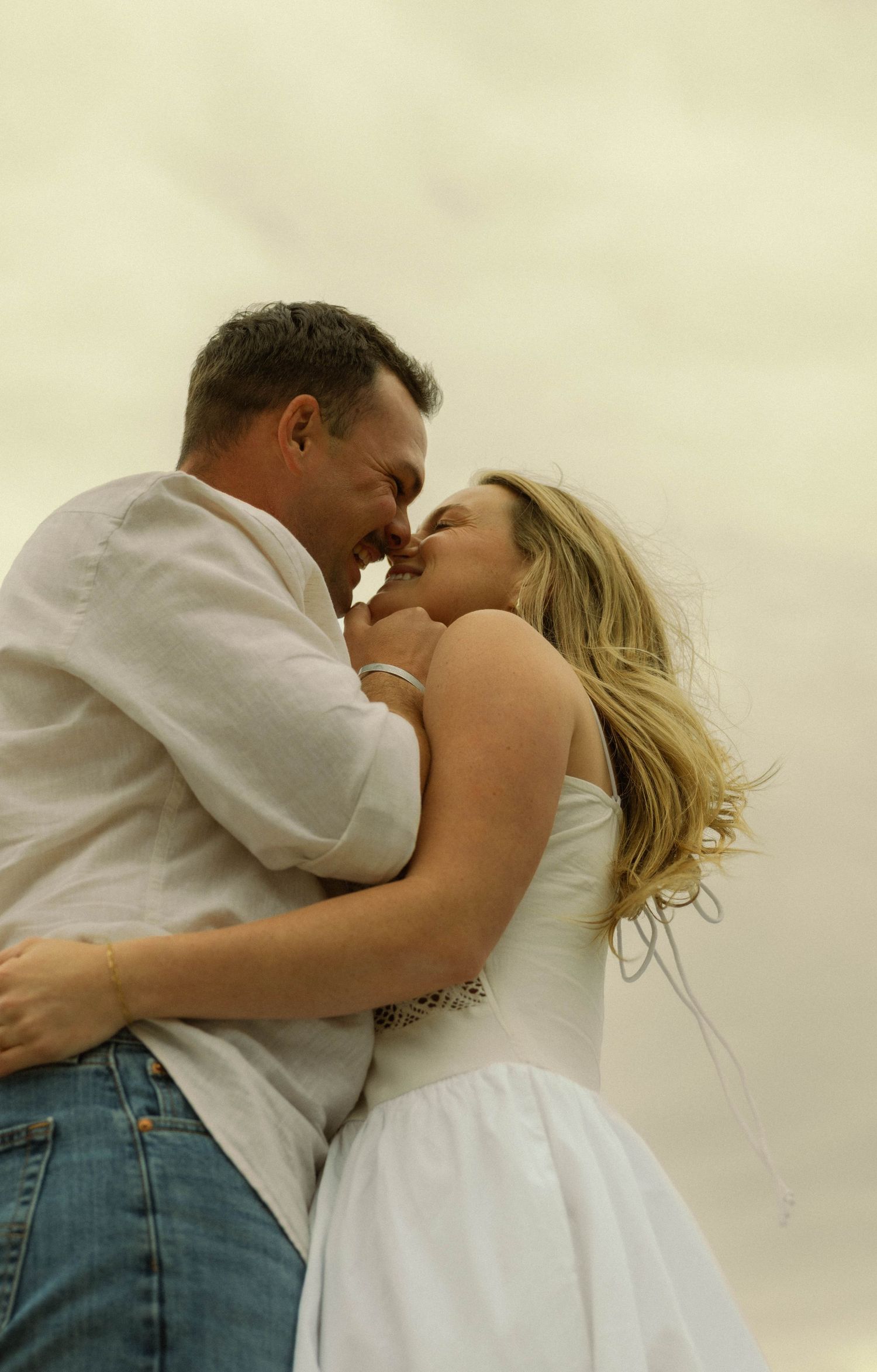A romantic couple in casual attire share an intimate embrace against a soft, dreamy background.