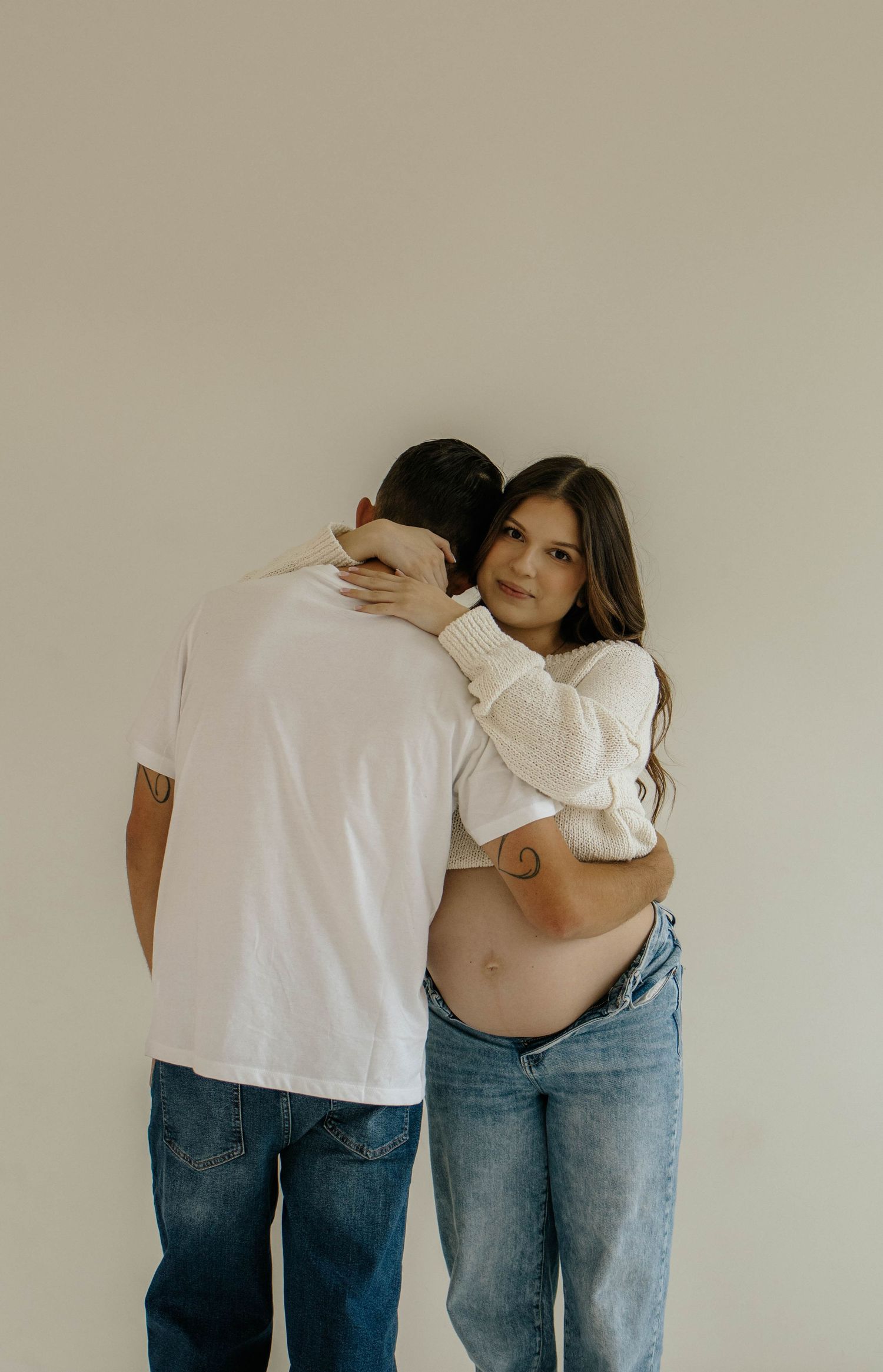 A series of romantic pregnancy photos showing gentle embraces against a light colored wall.
