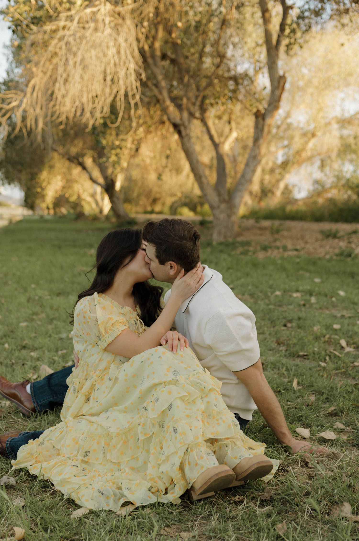 A tender moment captured between a couple lying on grass wearing yellow and white outfits.