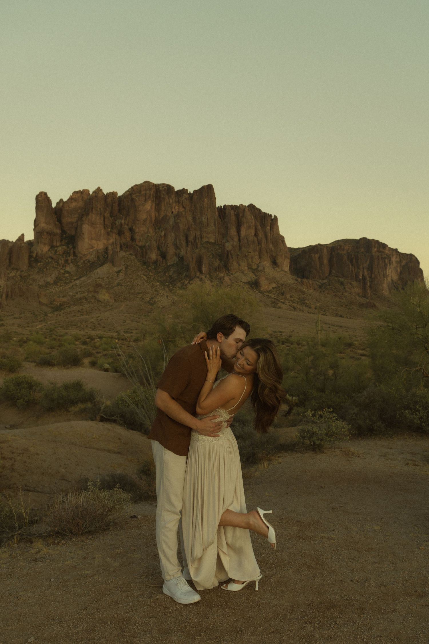Couple kissing passionately in desert landscape with Superstition Mountains at dusk.
