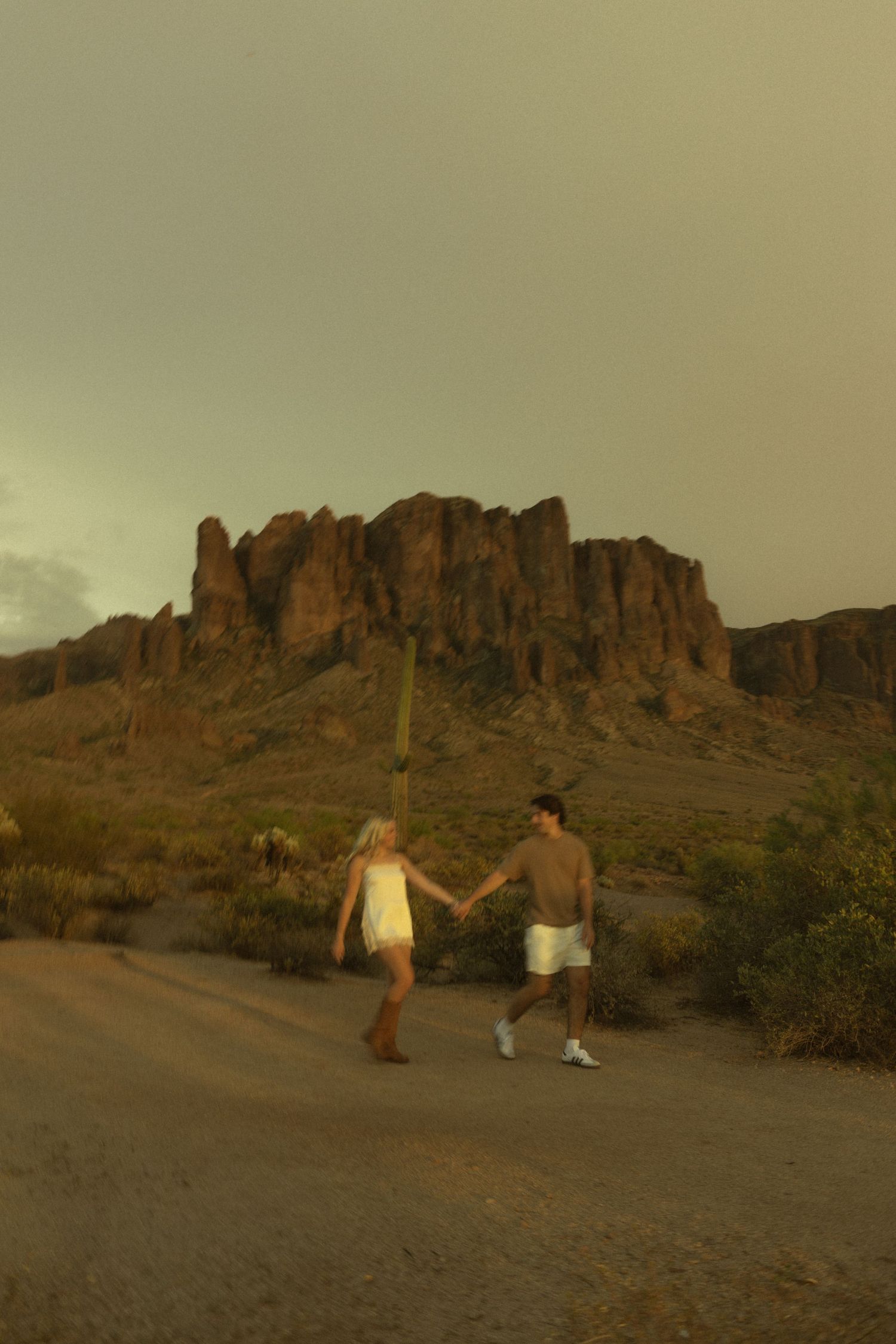 Couple holding hands walking on desert path with Superstition Mountains at sunset.