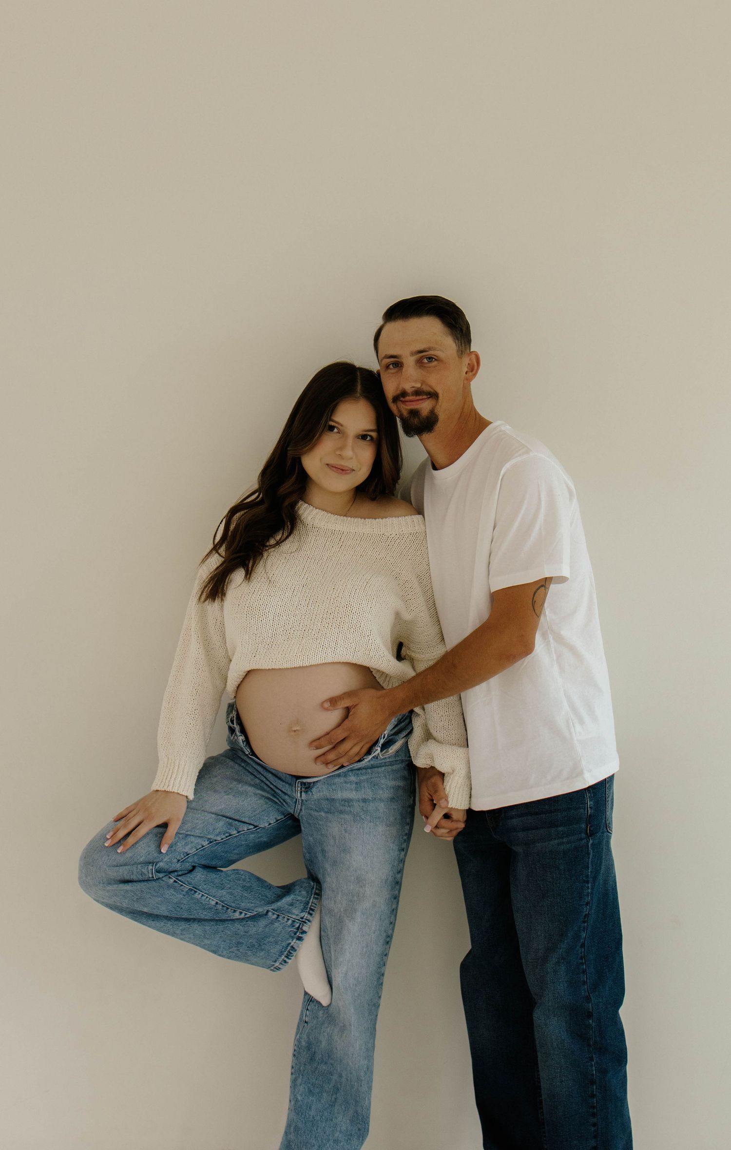 A couple in jeans and white tops share tender moments in a series of minimalist photos against a light background.