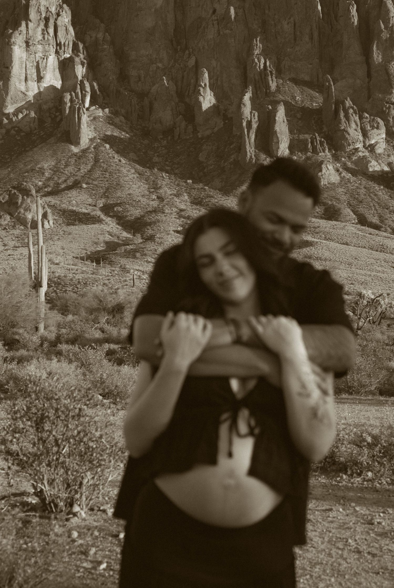 Four black and white photos show a couple embracing and dancing together in a natural outdoor setting with mountains.