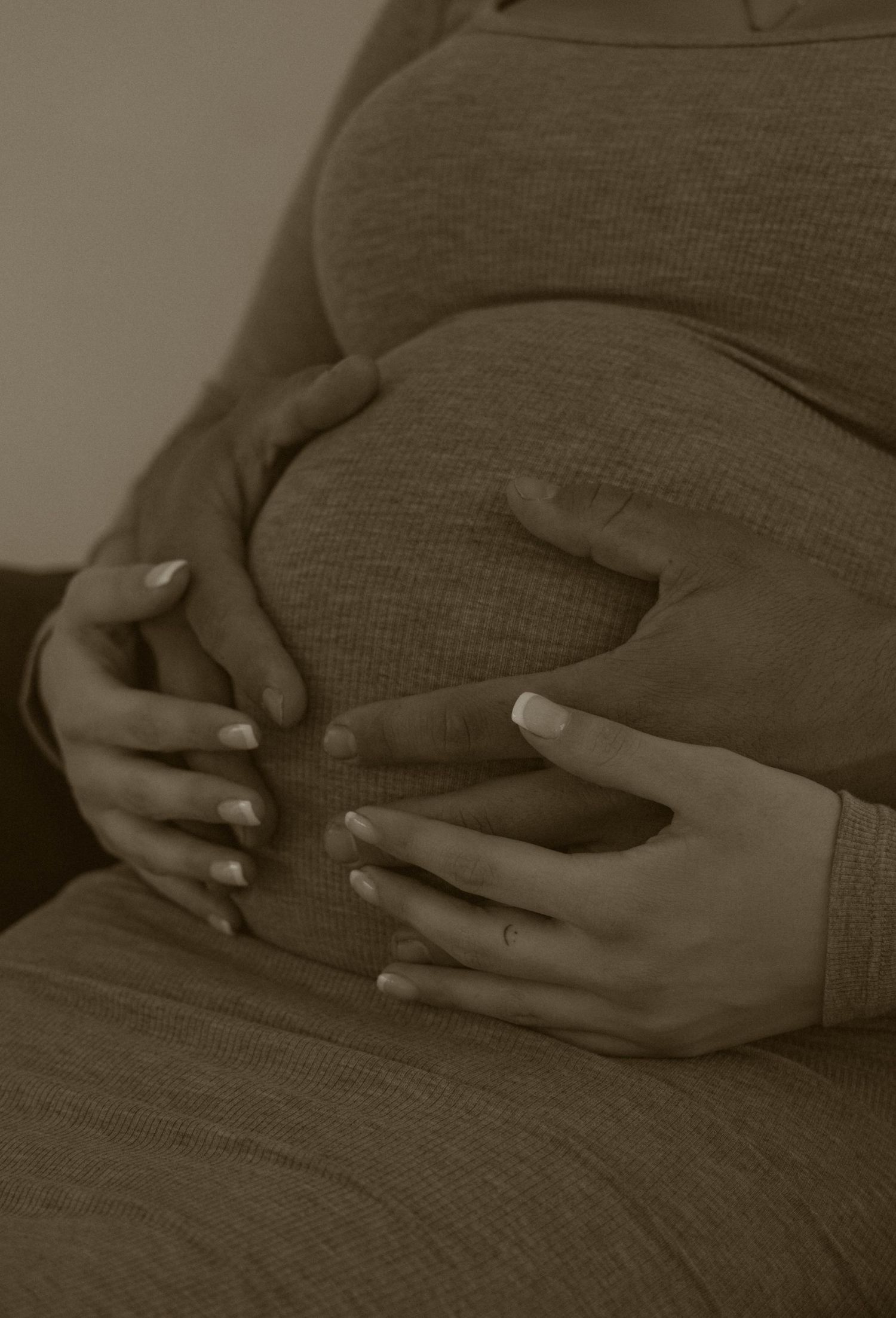 Close-up shots of hands tenderly cradling a pregnant belly in a grey dress.