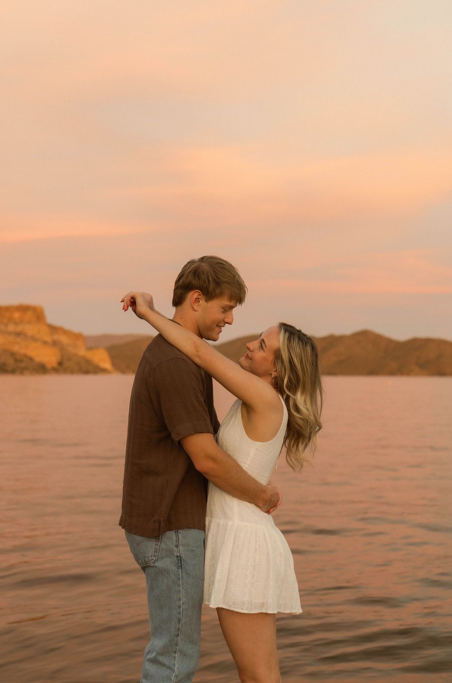 A romantic couple dances together by the water during a warm desert sunset.