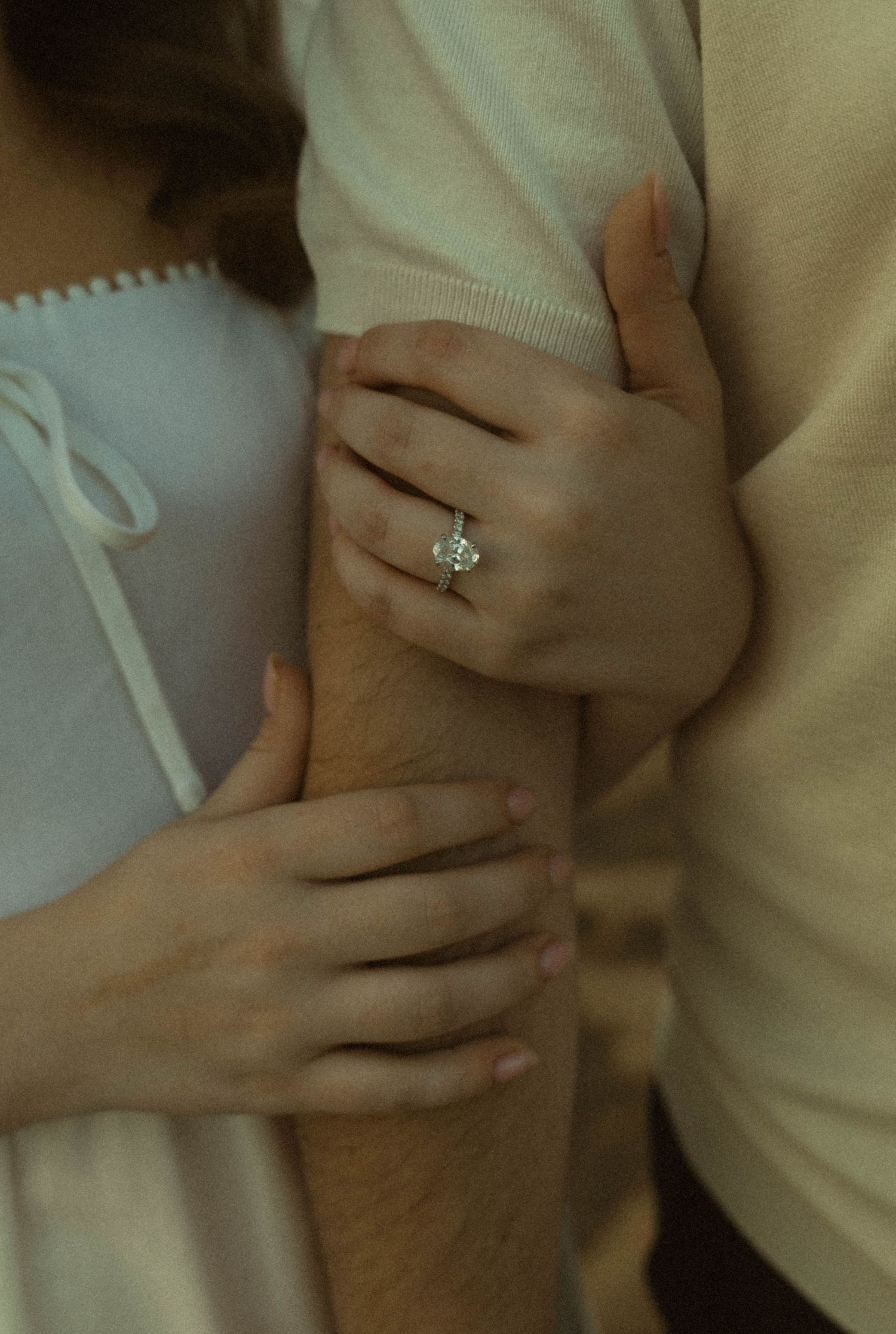 Close-up of woman's hand with diamond engagement ring wrapped around man's arm.