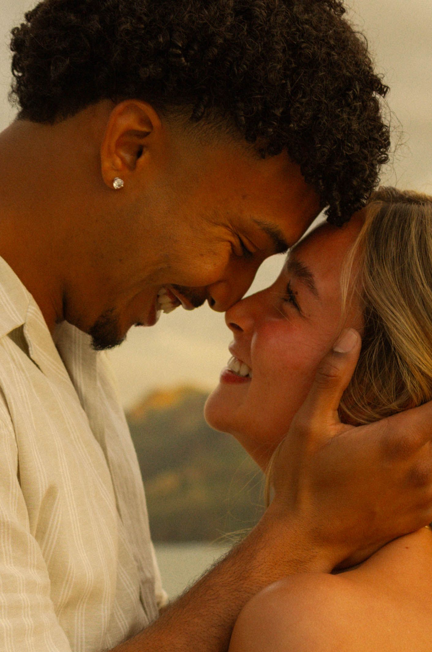 A romantic couple shares an intimate moment at sunset against a warm golden backdrop.