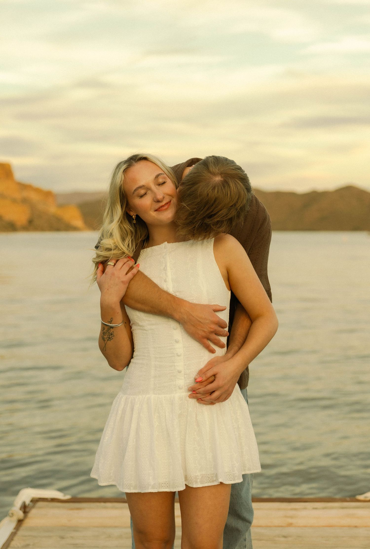 A tender moment captured between two people against a golden sunset over water.