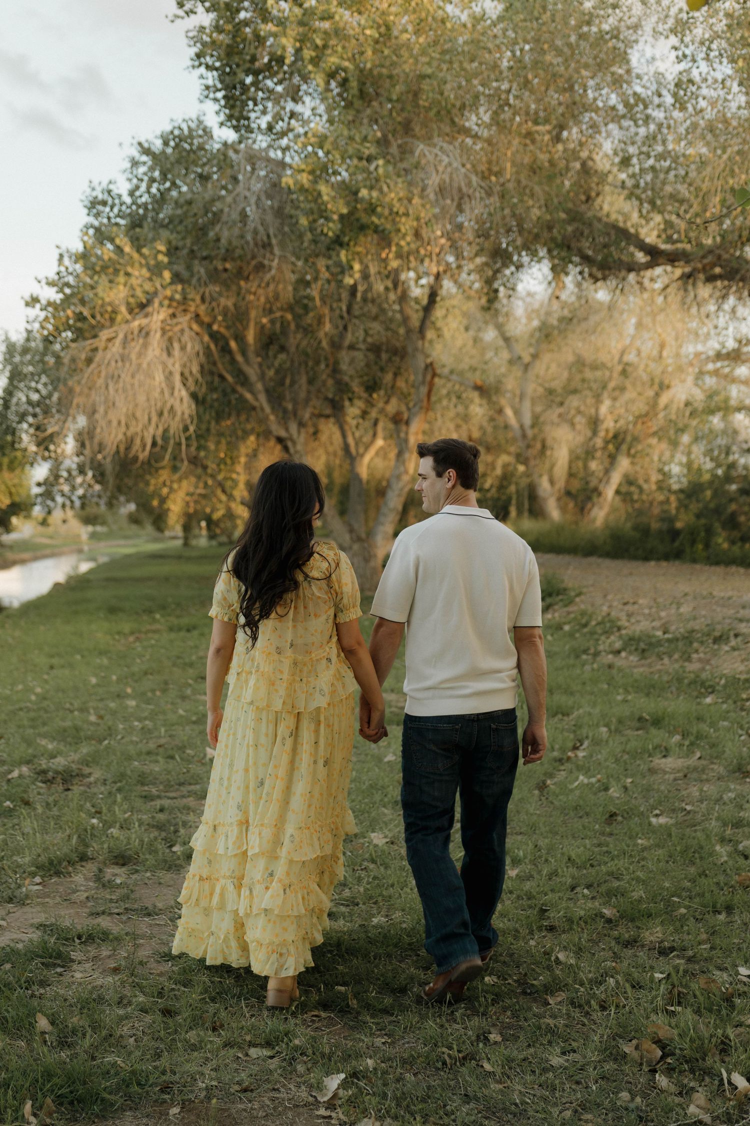 Couple walking together in a scenic autumn grove wearing yellow dress and white shirt.