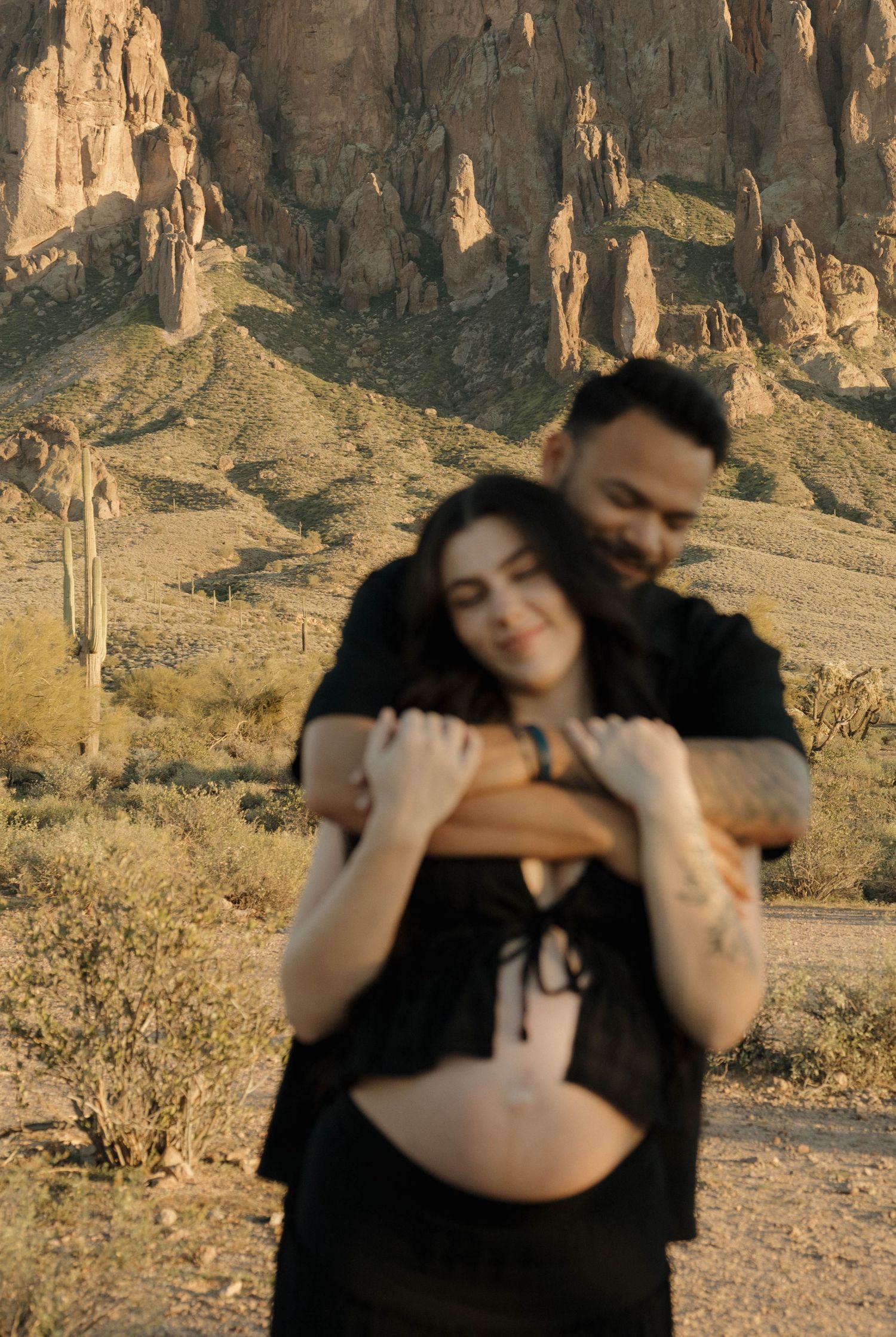 A couple shares an intimate moment in front of towering desert rock formations during golden hour.