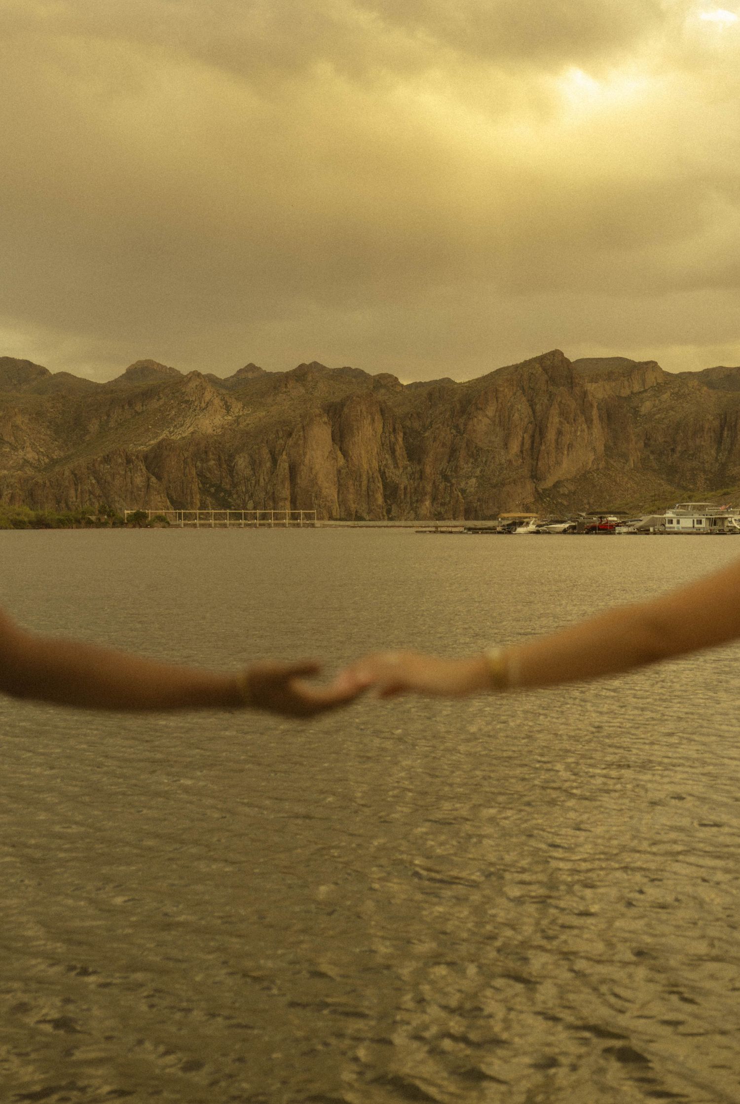 Couple holding hands on a serene lakeside dock with dramatic mountain scenery at golden hour.