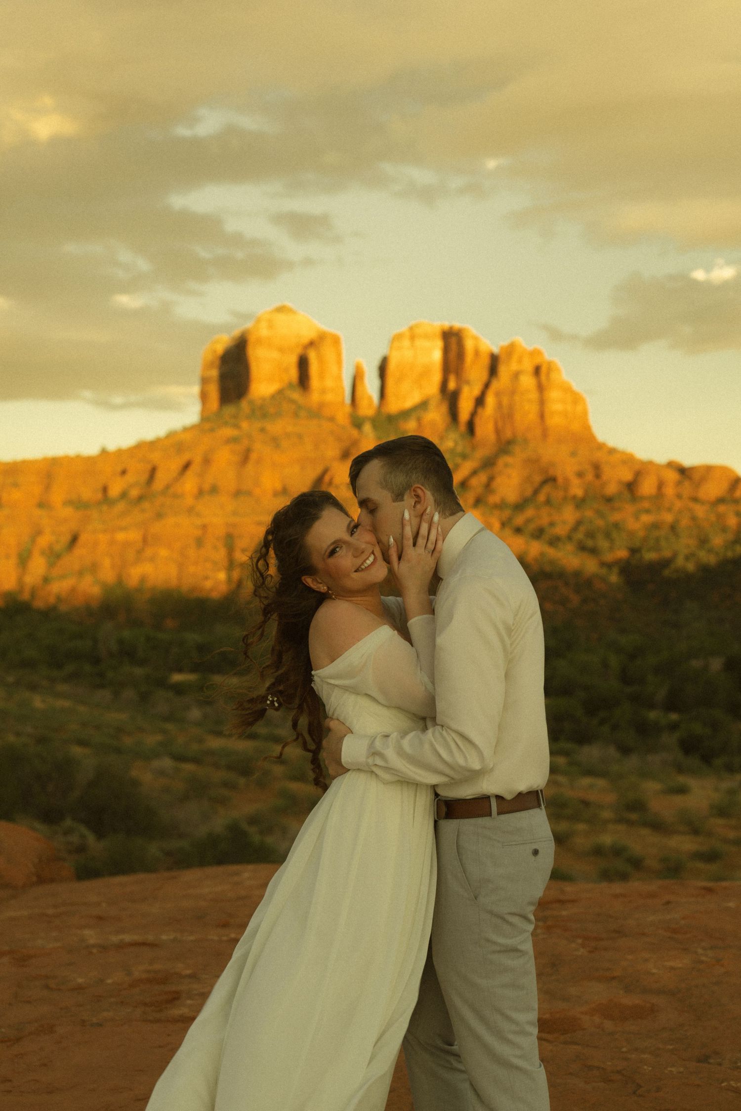 Couple sharing a romantic kiss at sunset with Cathedral Rock in Sedona, Arizona glowing golden in the background.