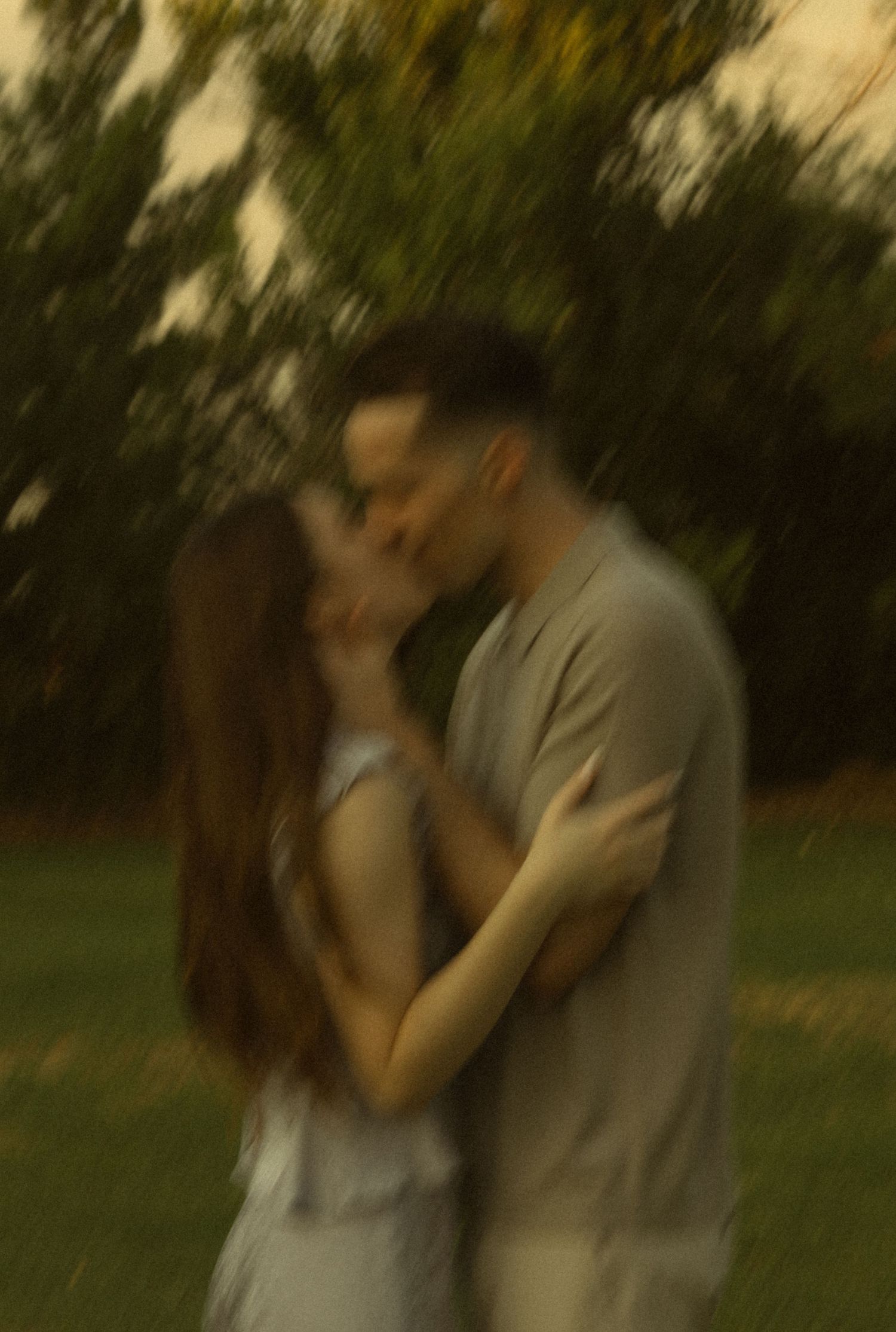 Couple sharing a romantic kiss outdoors in a dreamy blurred garden setting at dusk.