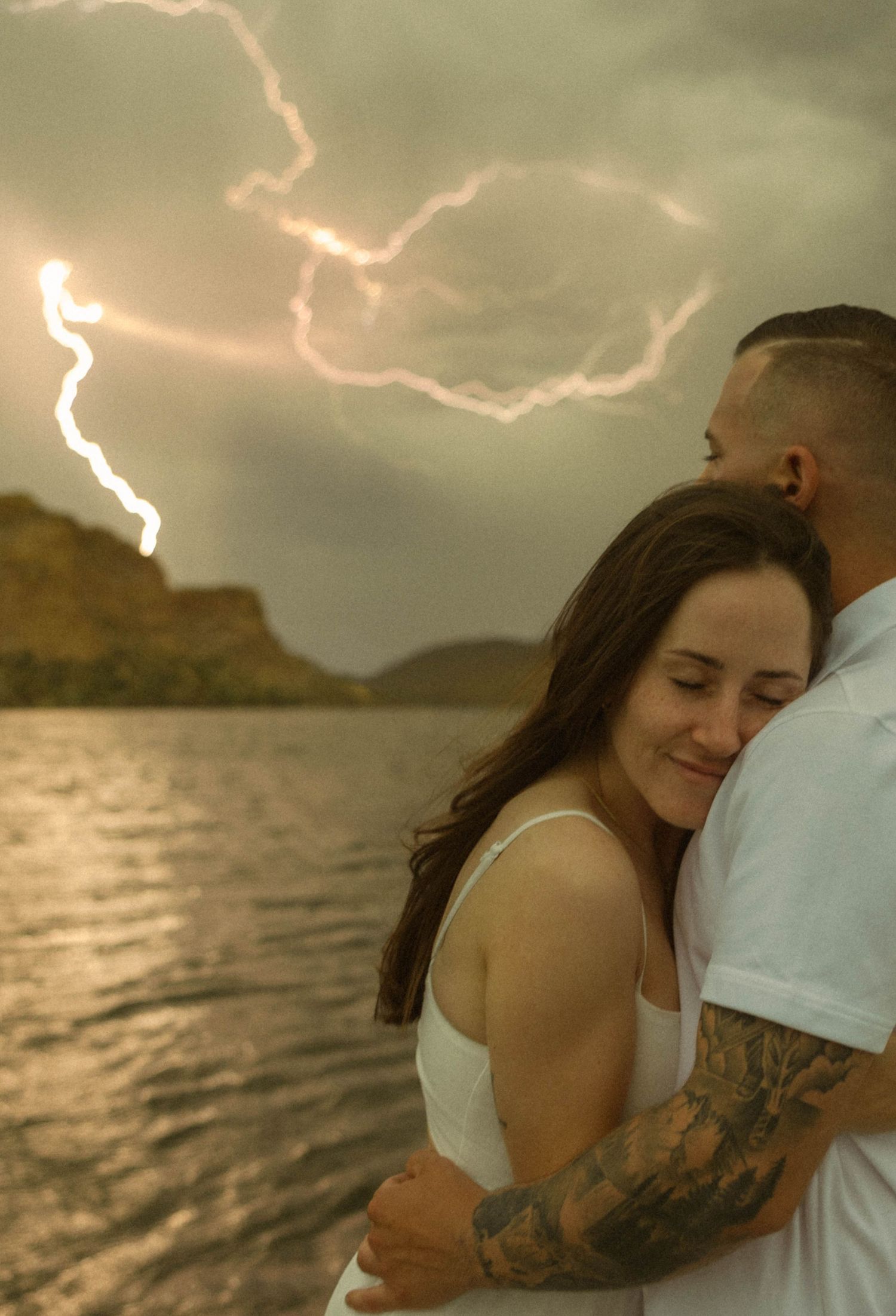 Dramatic lightning illuminates a couple's tender embrace by the ocean at dusk.