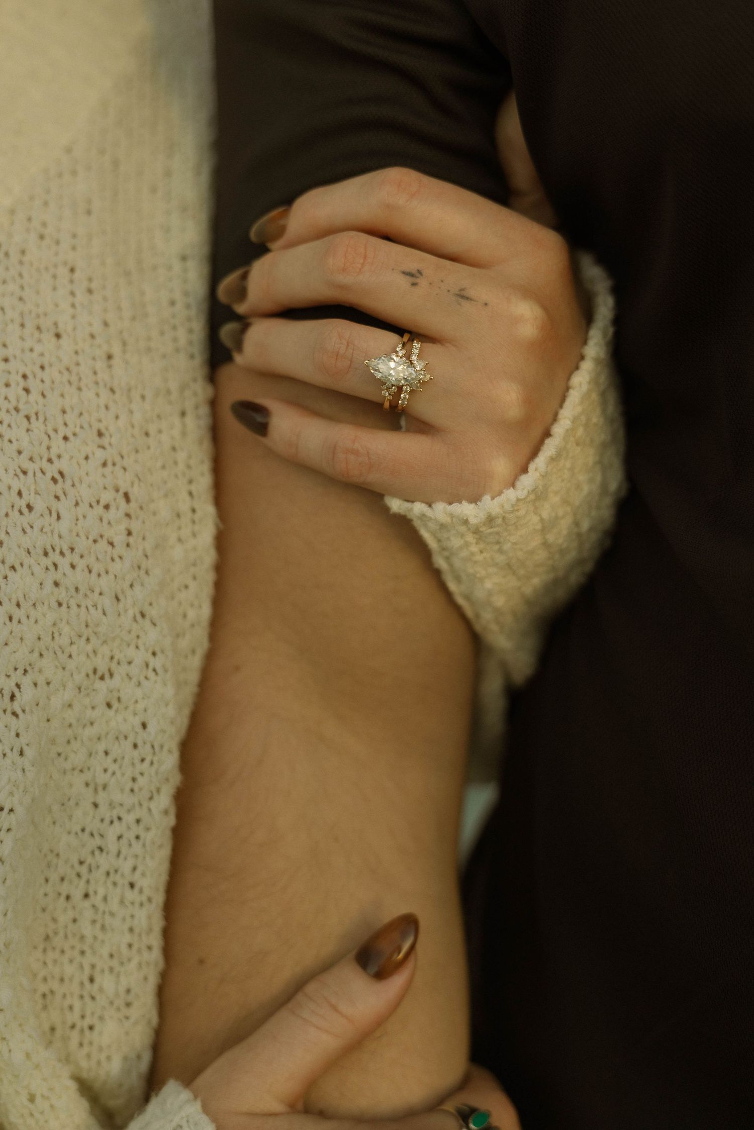 Close-up of a hand wearing a sparkling diamond engagement ring and cozy cream sweater sleeve.