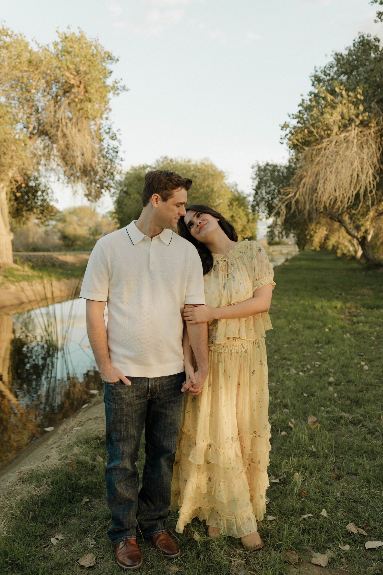 A couple shares an intimate moment beside a large tree trunk in a sunlit meadow.