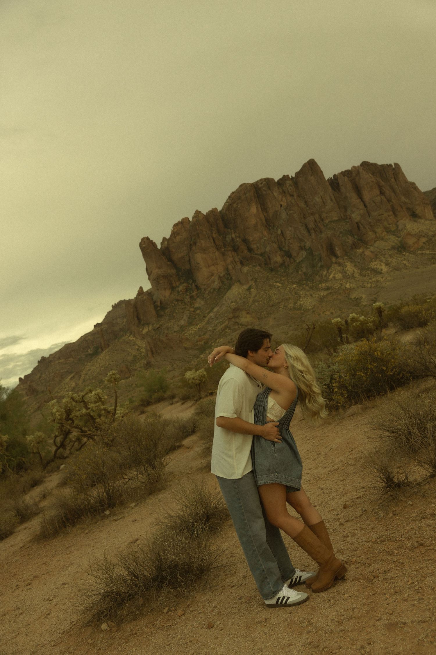 Couple kissing in the Arizona desert with dramatic rocky Superstition Mountains in the background.
