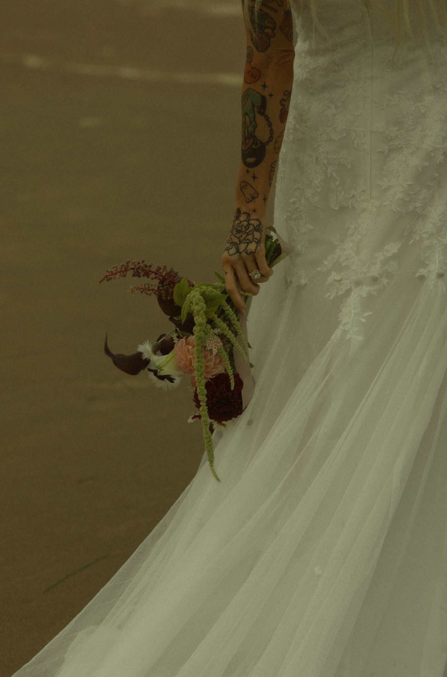 Tattooed bride in white lace wedding gown holding a unique dark floral bouquet with green accents.