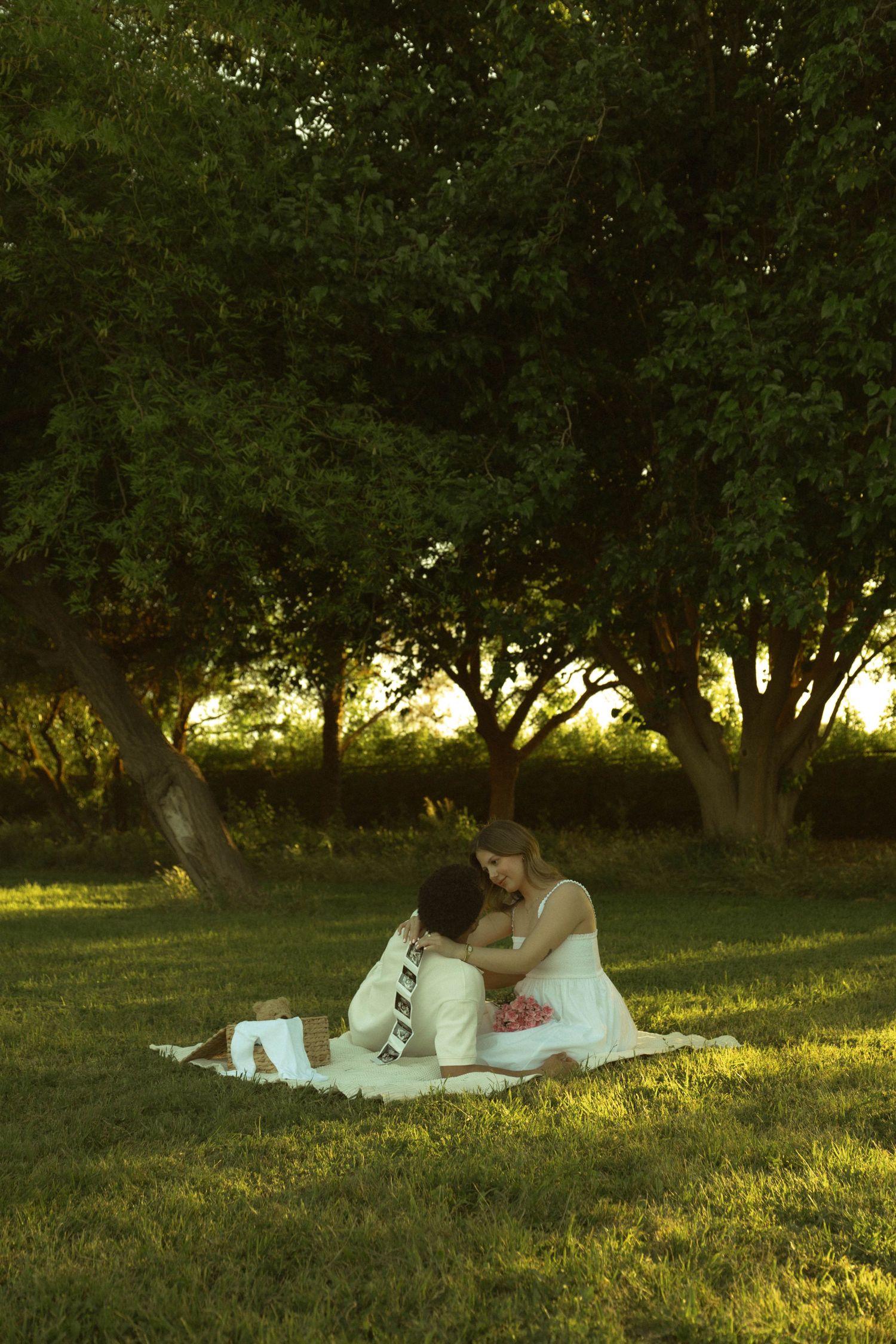 Couple sharing a romantic embrace on a blanket in a lush green park at golden hour sunset.