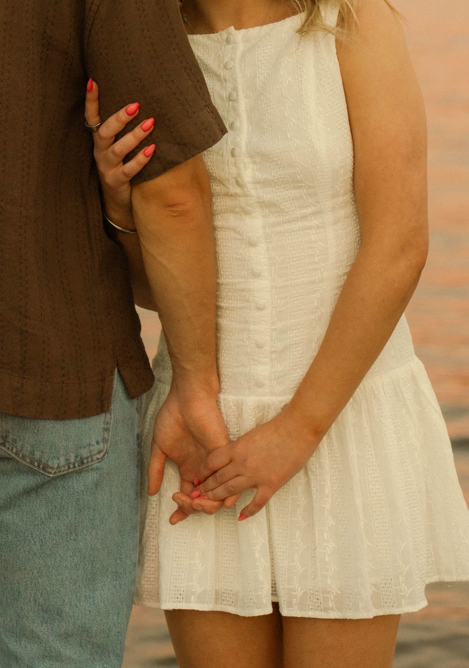 Close-up details of a couple in casual summer attire showing affectionate body language against a warm sunset.