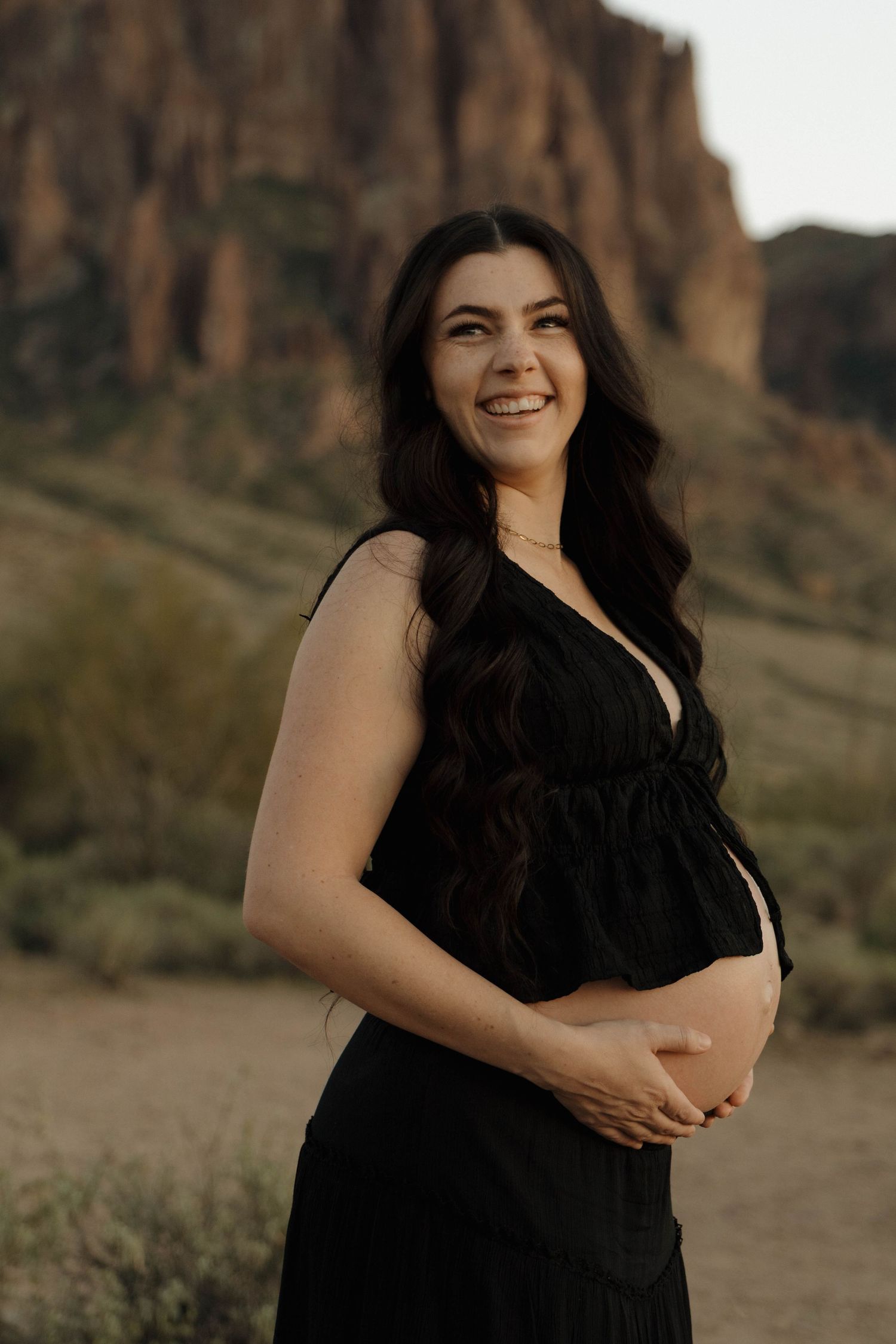 A person in a black dress poses confidently against a backdrop of dramatic red rock cliffs at sunset.