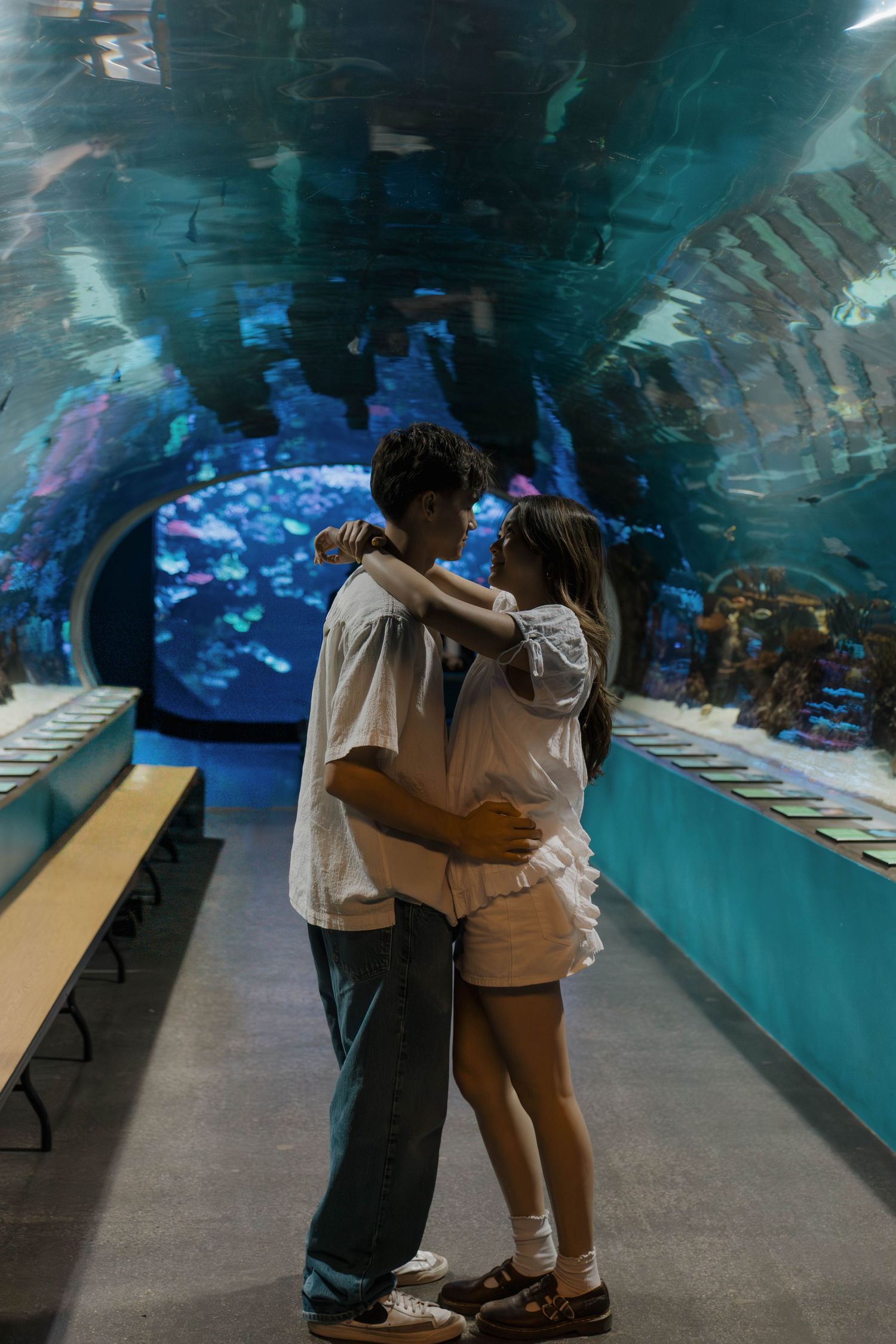 Two people embrace in front of a blue-lit aquarium display.