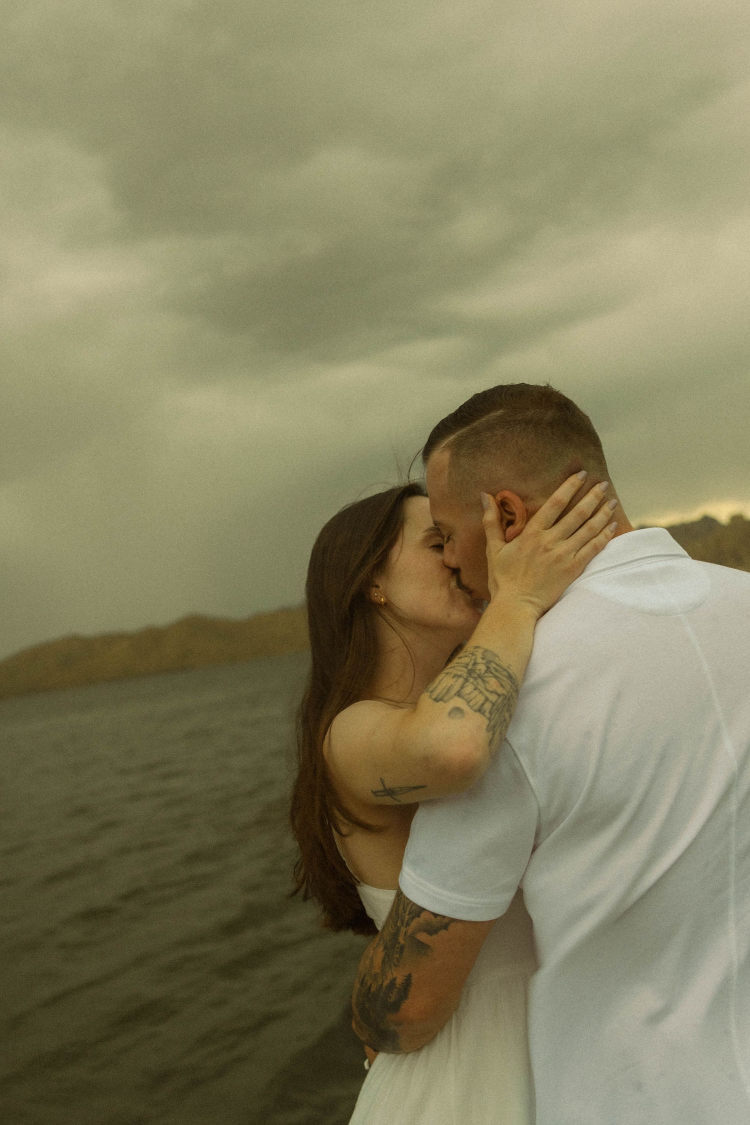 Couple shares an intimate moment against stormy skies and ocean waves.