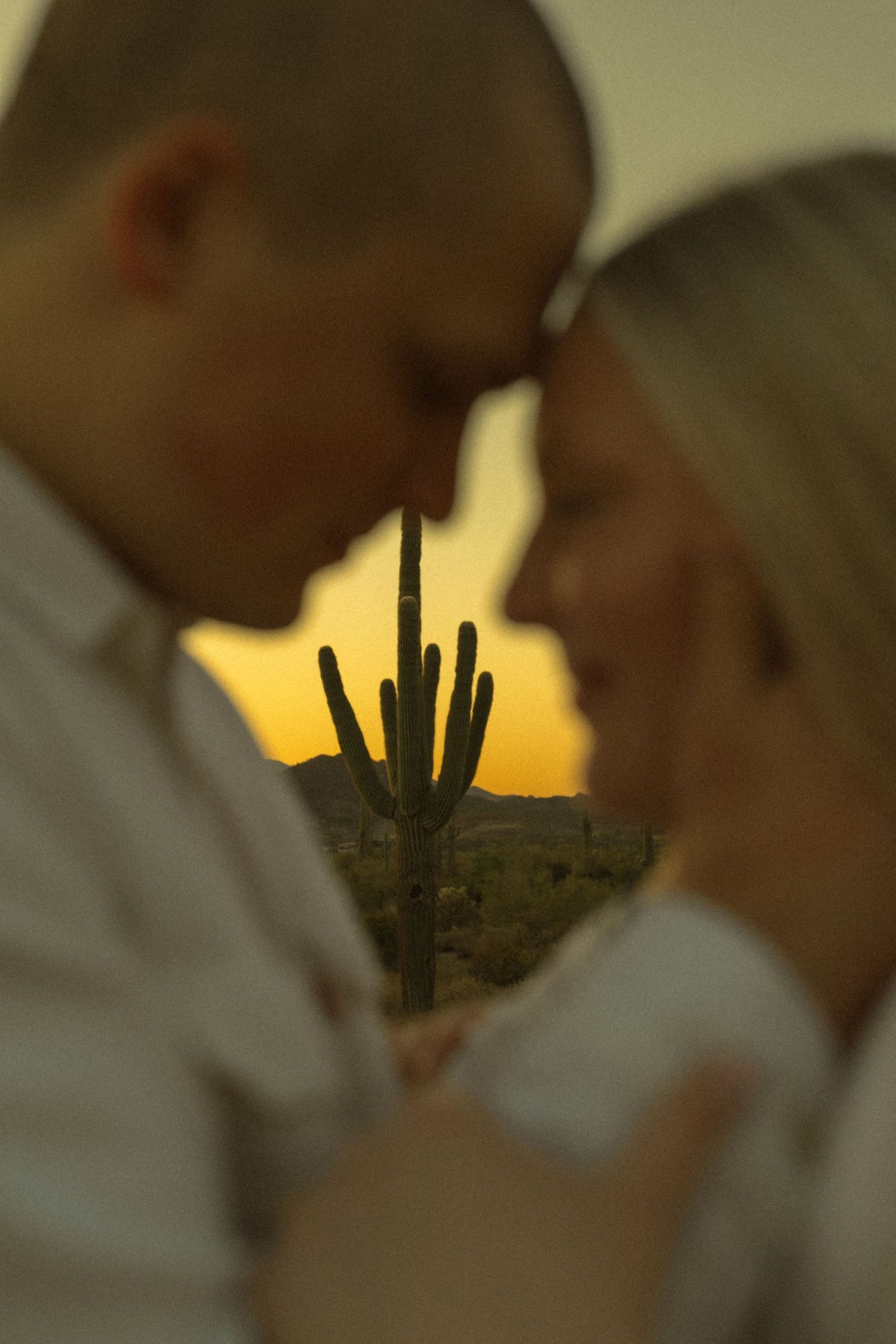 Couple touching foreheads at sunset with saguaro cactus silhouette in Arizona desert background.