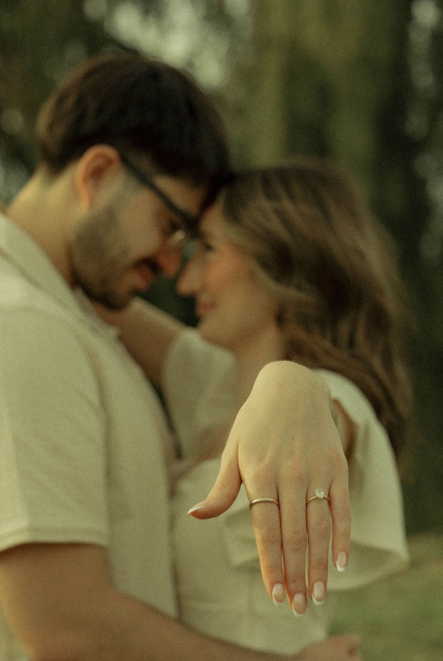 Couple sharing a romantic moment outdoors, woman displaying an engagement ring on her outstretched hand.
