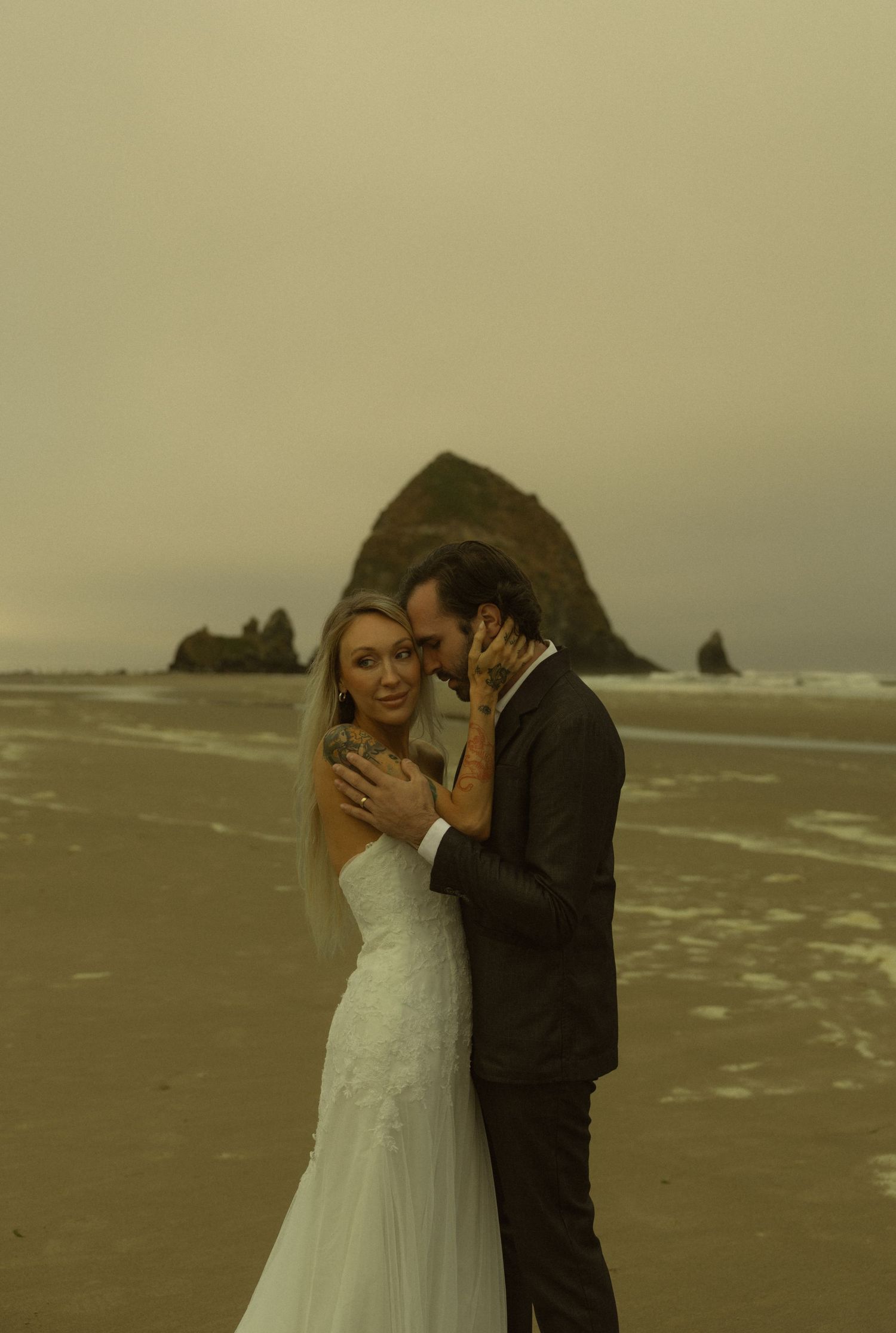 Bride and groom embrace on Cannon Beach with Haystack Rock backdrop on a moody, overcast day.