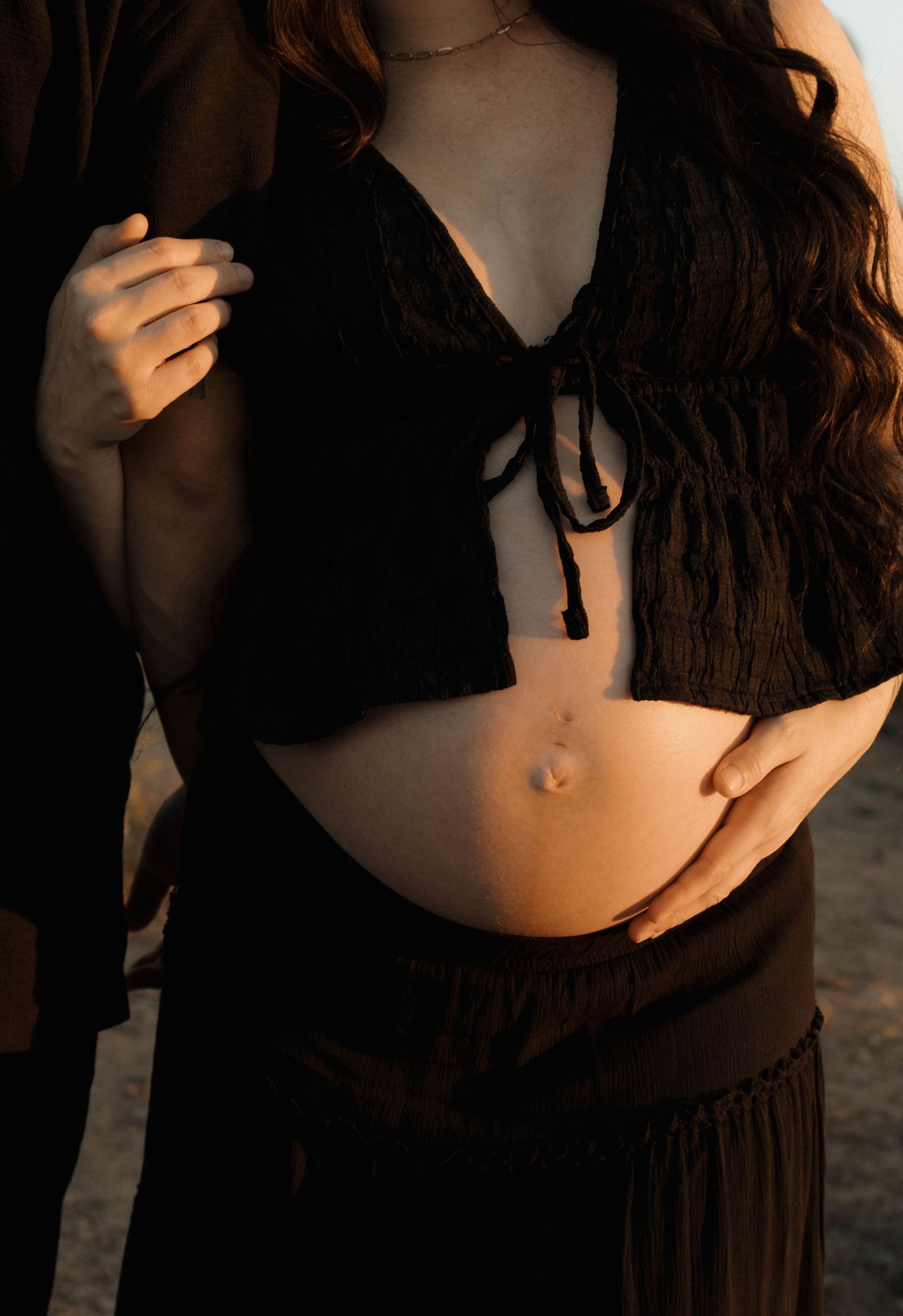 Close-up maternity photography showing artistic angles of a black dress against a natural backdrop.