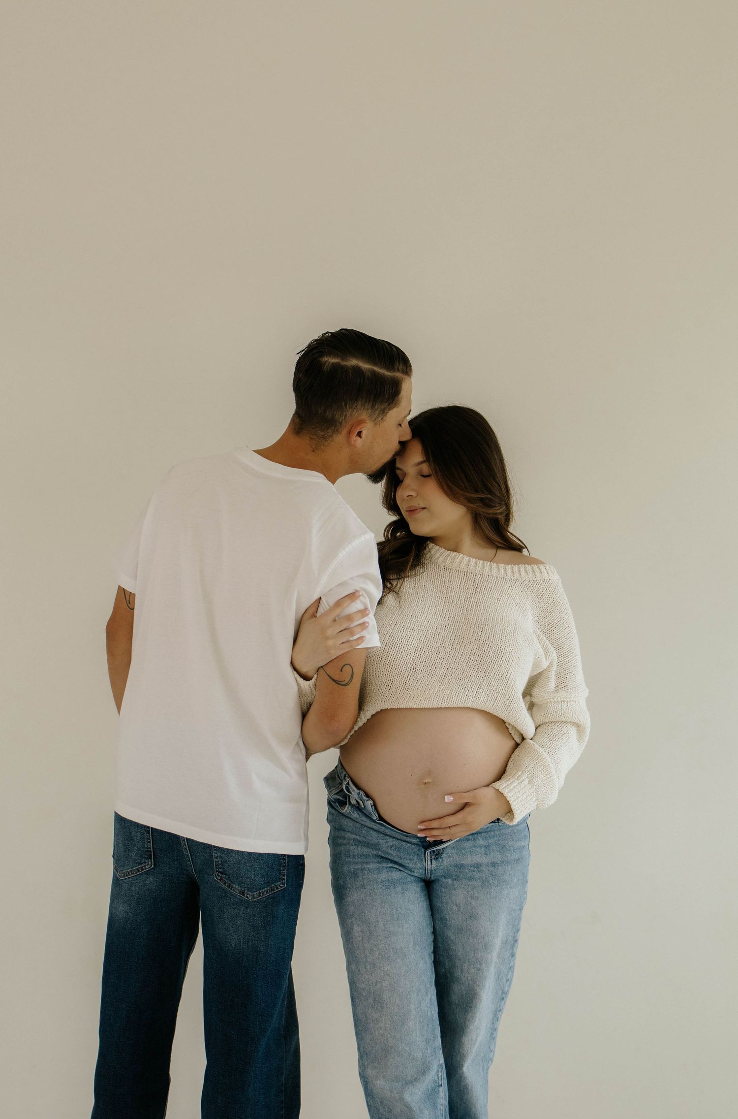 A series of intimate maternity photos showing a couple embracing against a neutral background.