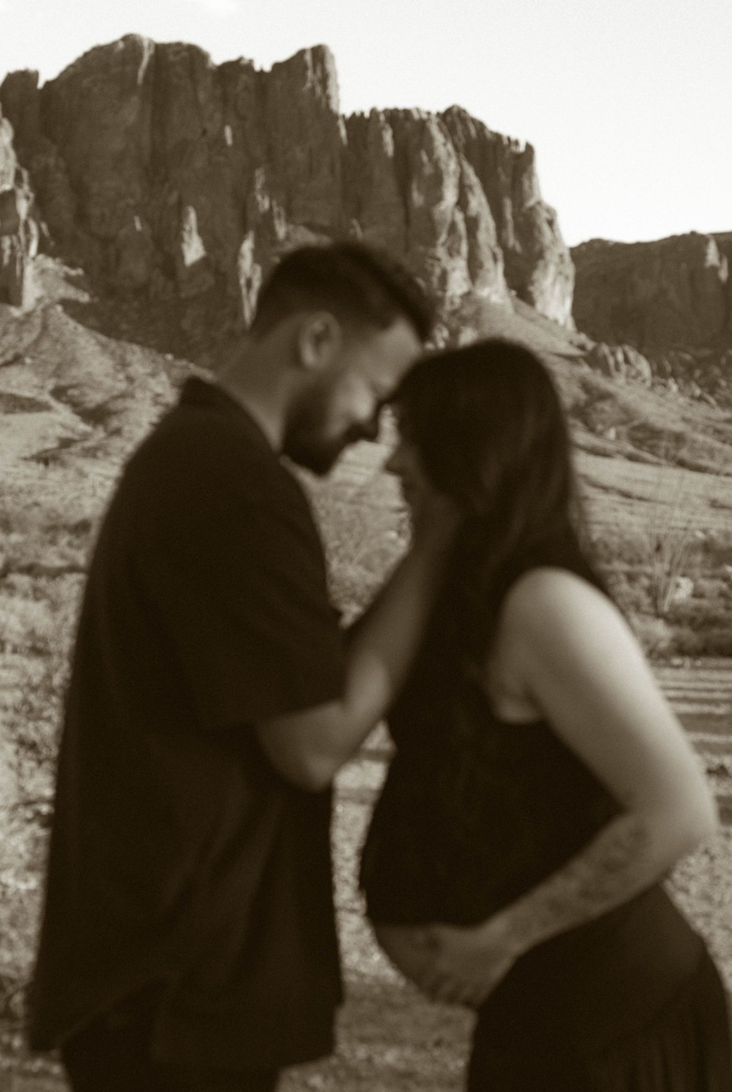 A series of five sepia-toned photographs showing a couple embracing against a dramatic desert cliff backdrop.