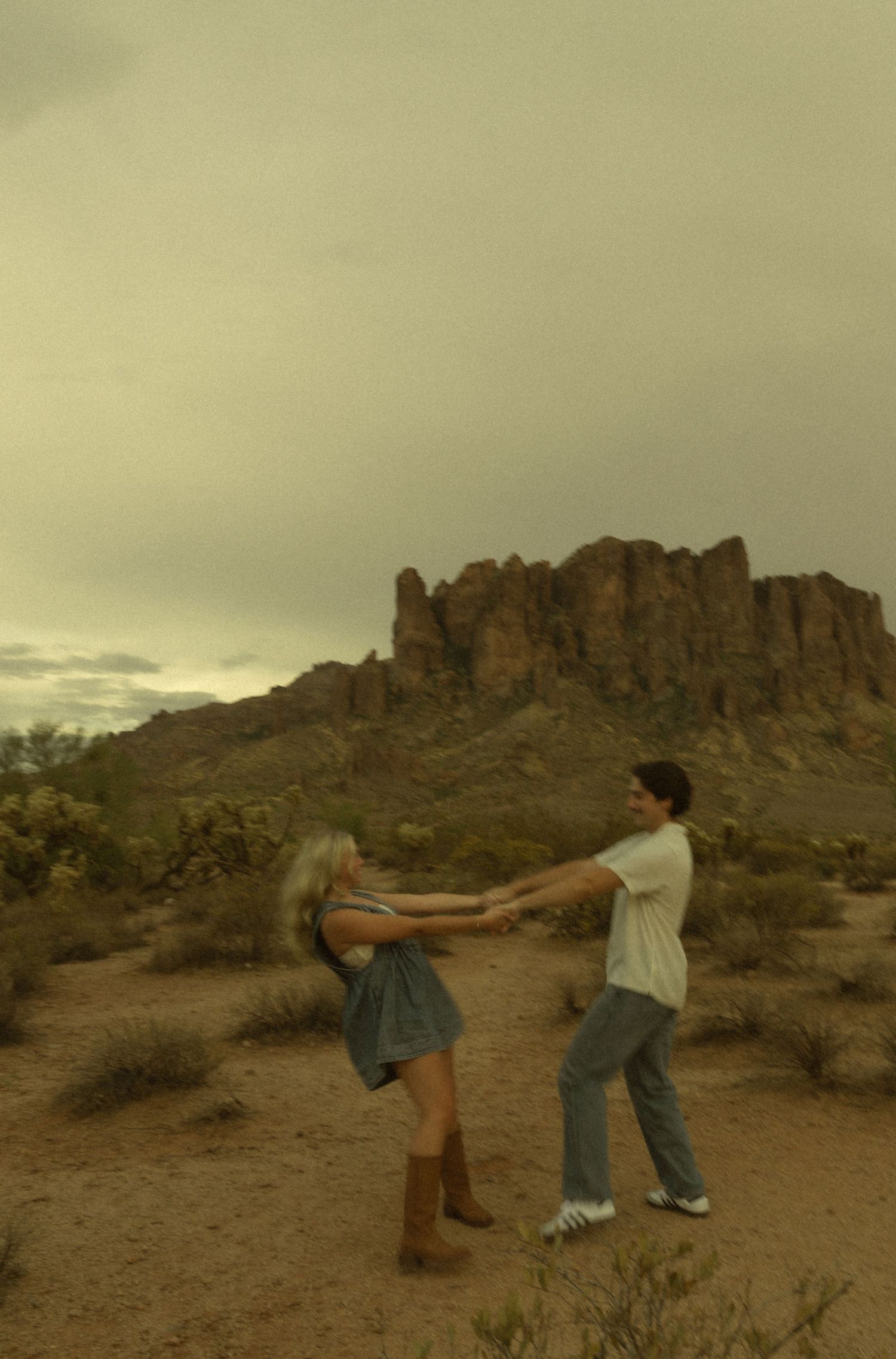 Couple dancing and spinning together in the desert with rugged mountain formations behind them.