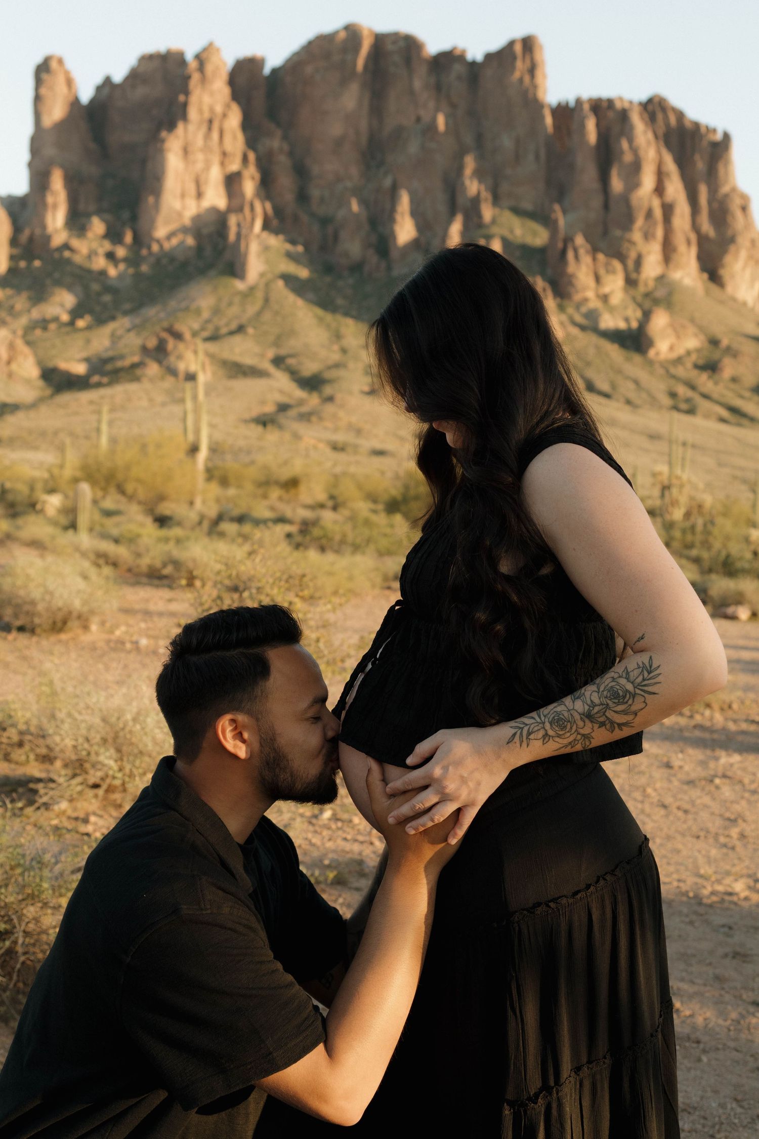 A romantic couple shares intimate moments in a desert landscape with dramatic rock formations at sunset.
