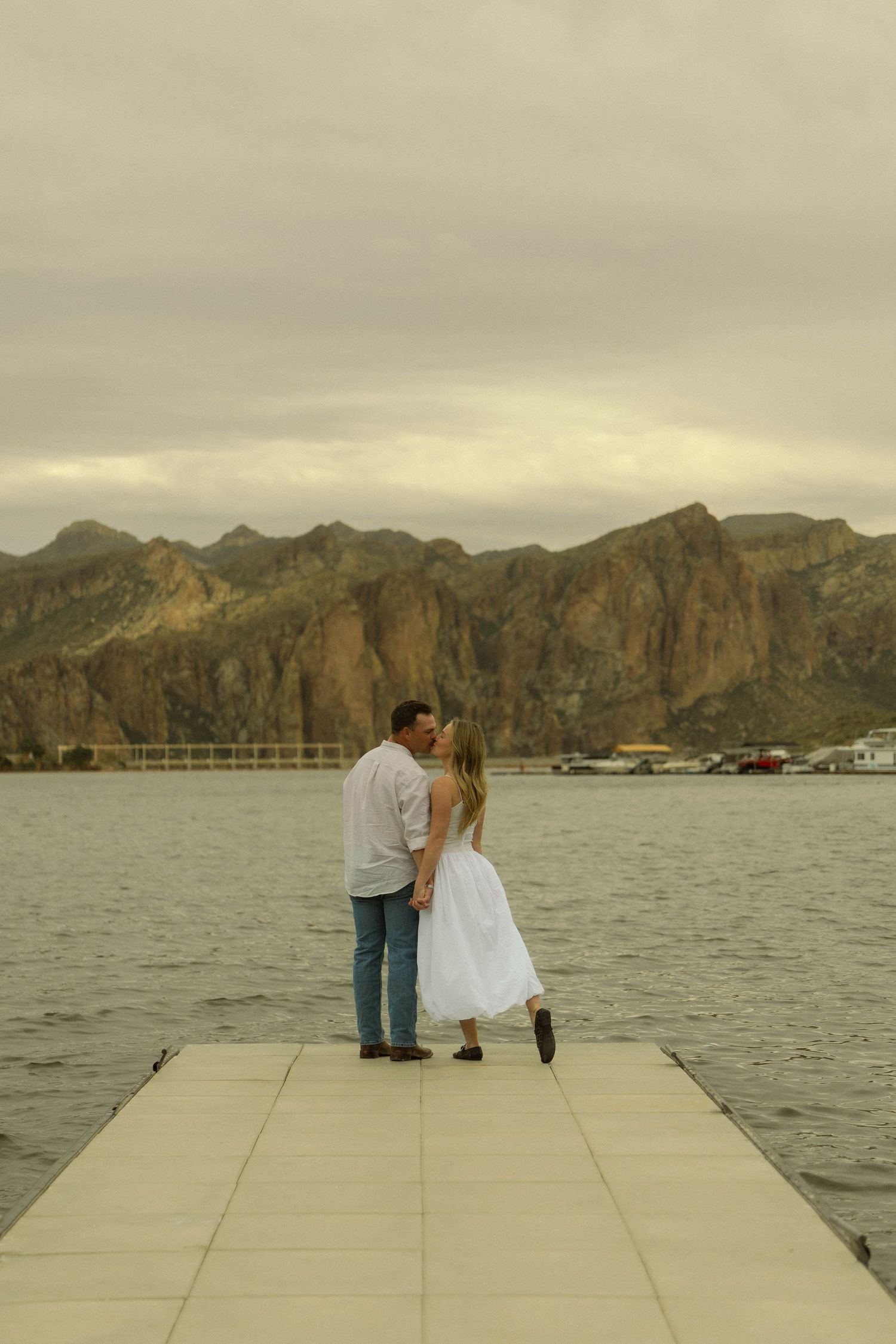 Couple shares intimate moment on dock with mountainous landscape in background.