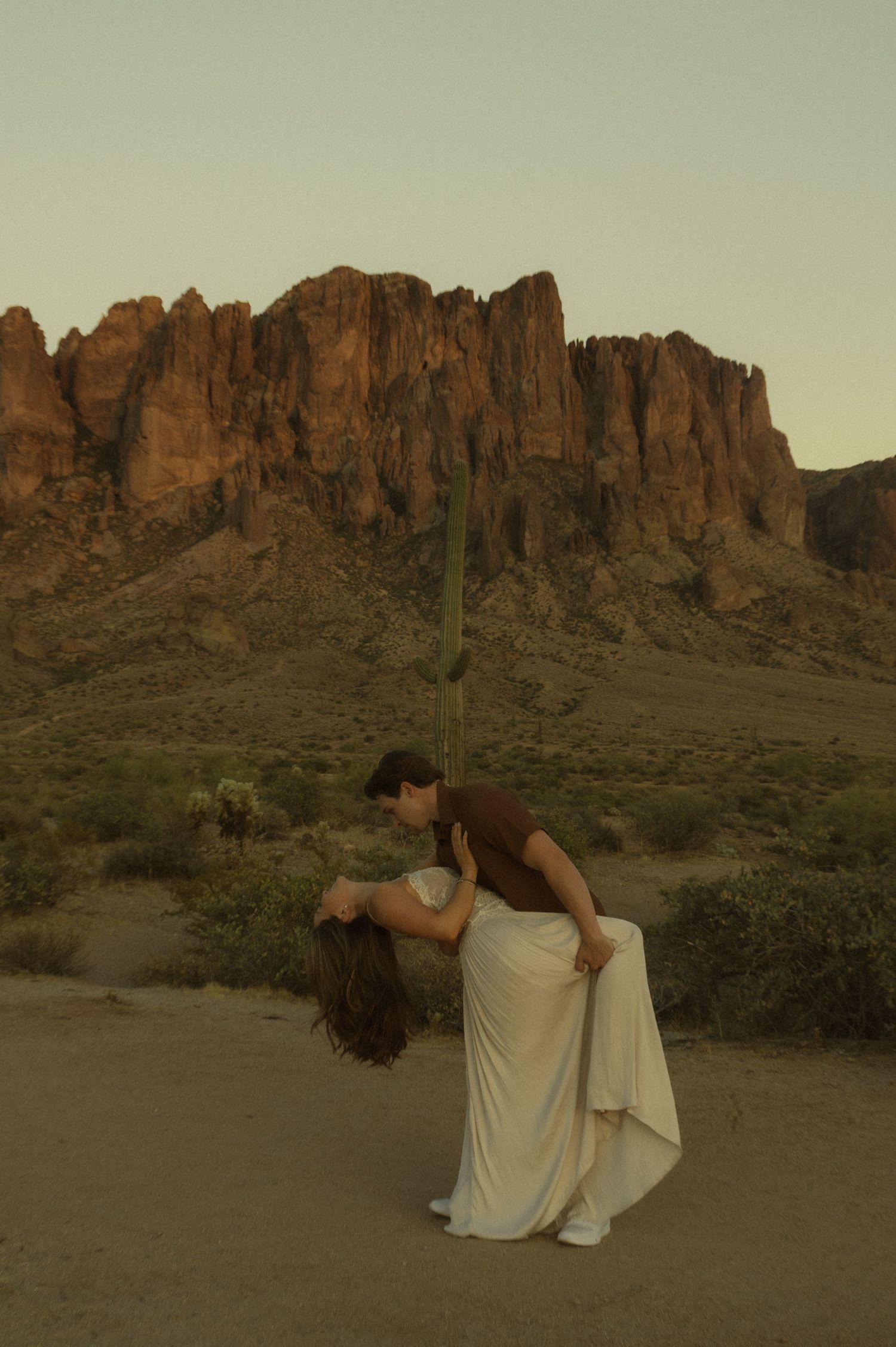 Couple sharing a romantic dip kiss in the Arizona desert with Superstition Mountains at golden hour.