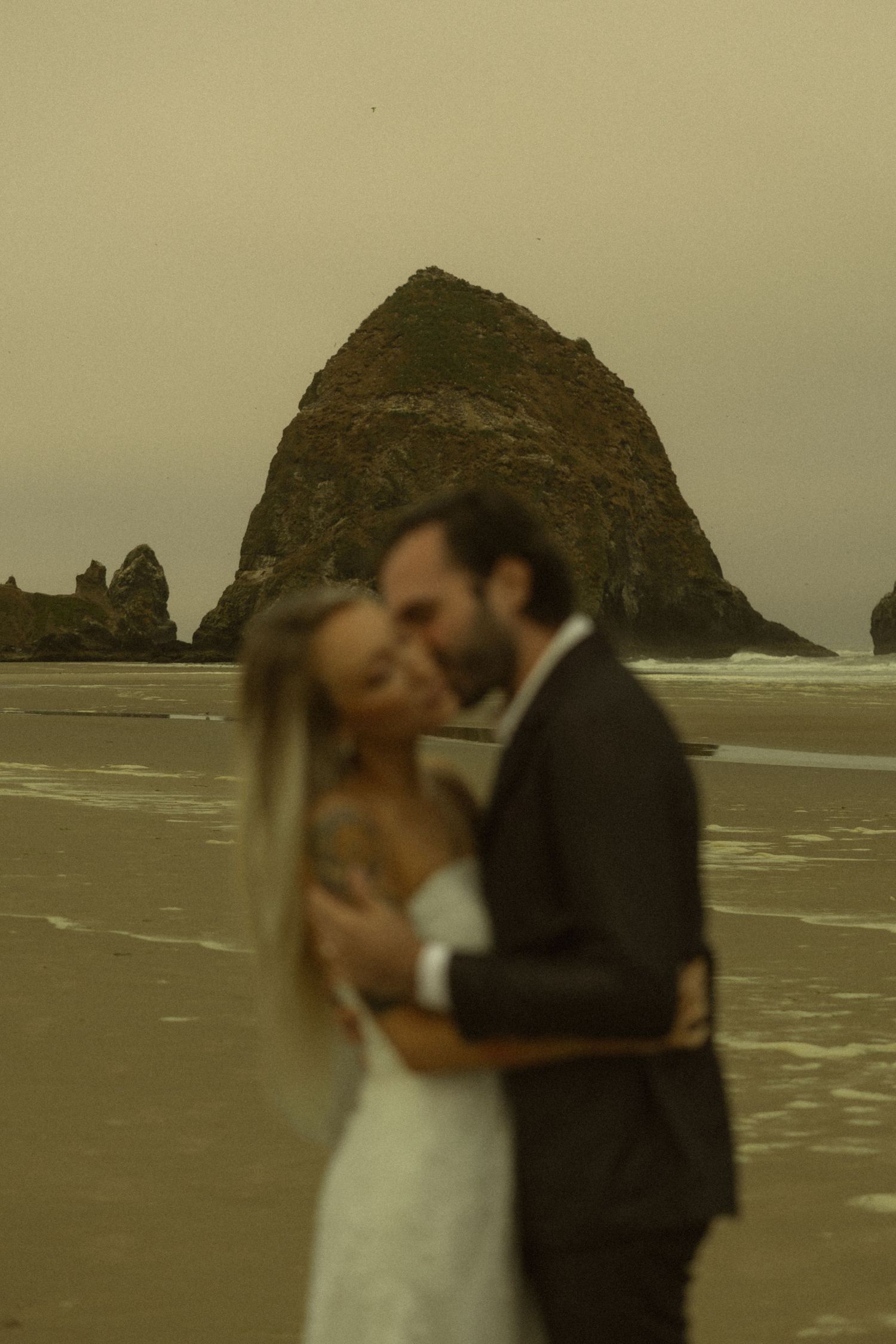 Couple embracing on Cannon Beach with iconic Haystack Rock in background during golden hour wedding photo.