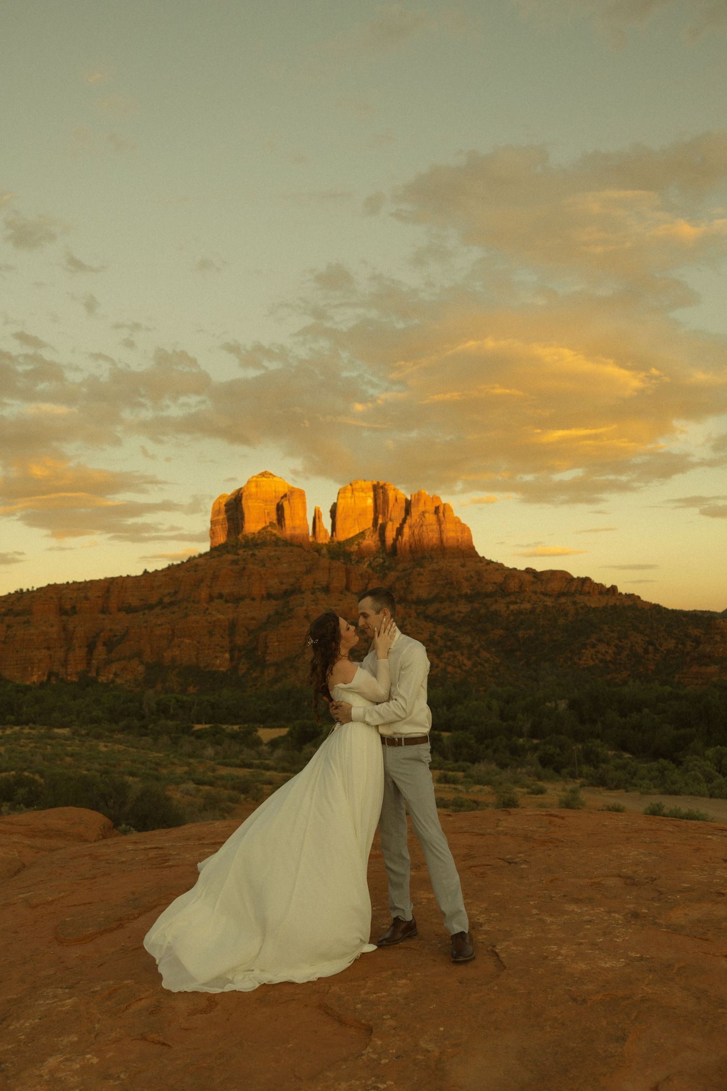 Couple sharing a romantic kiss at sunset with Cathedral Rock in Sedona, Arizona glowing golden in the background.